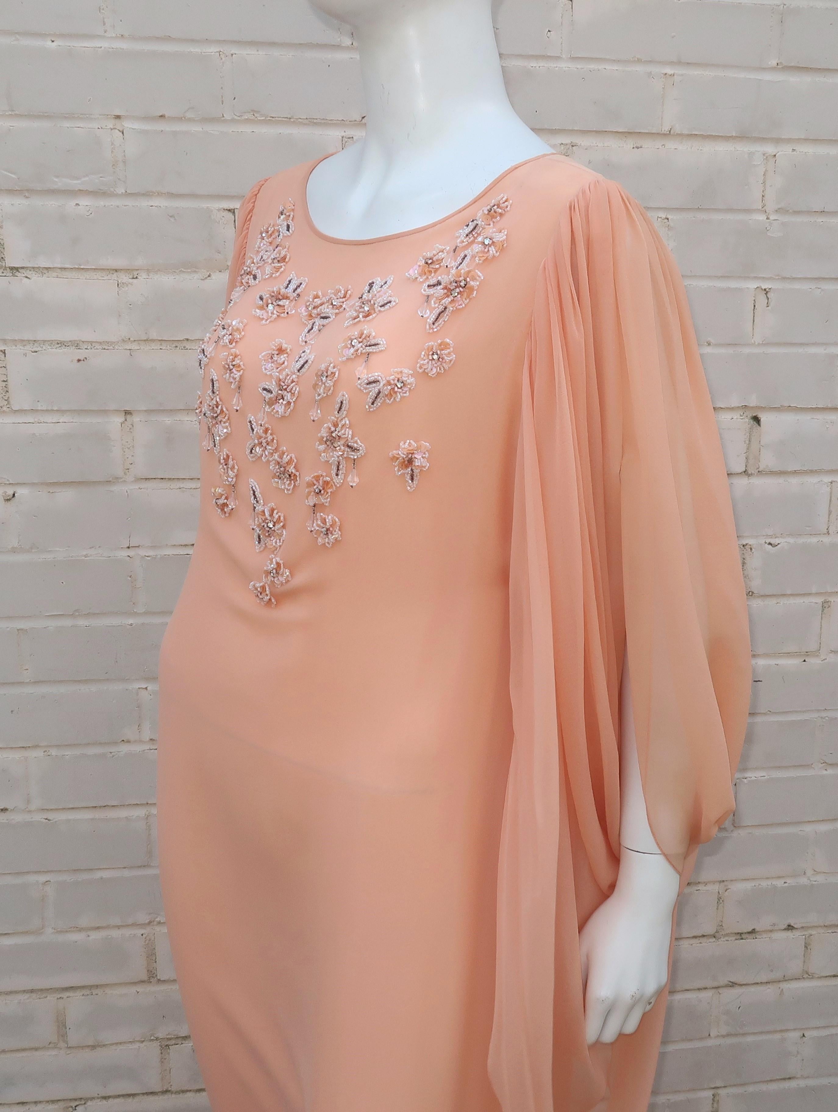 The ethereal silhouette of this 1970's pale peach chiffon Richilene evening dress is worthy of a modern day goddess.  The dress zips and hooks at the back with dramatic draped sleeves that provide 'wings' and a cocooned effect.  The white and silver