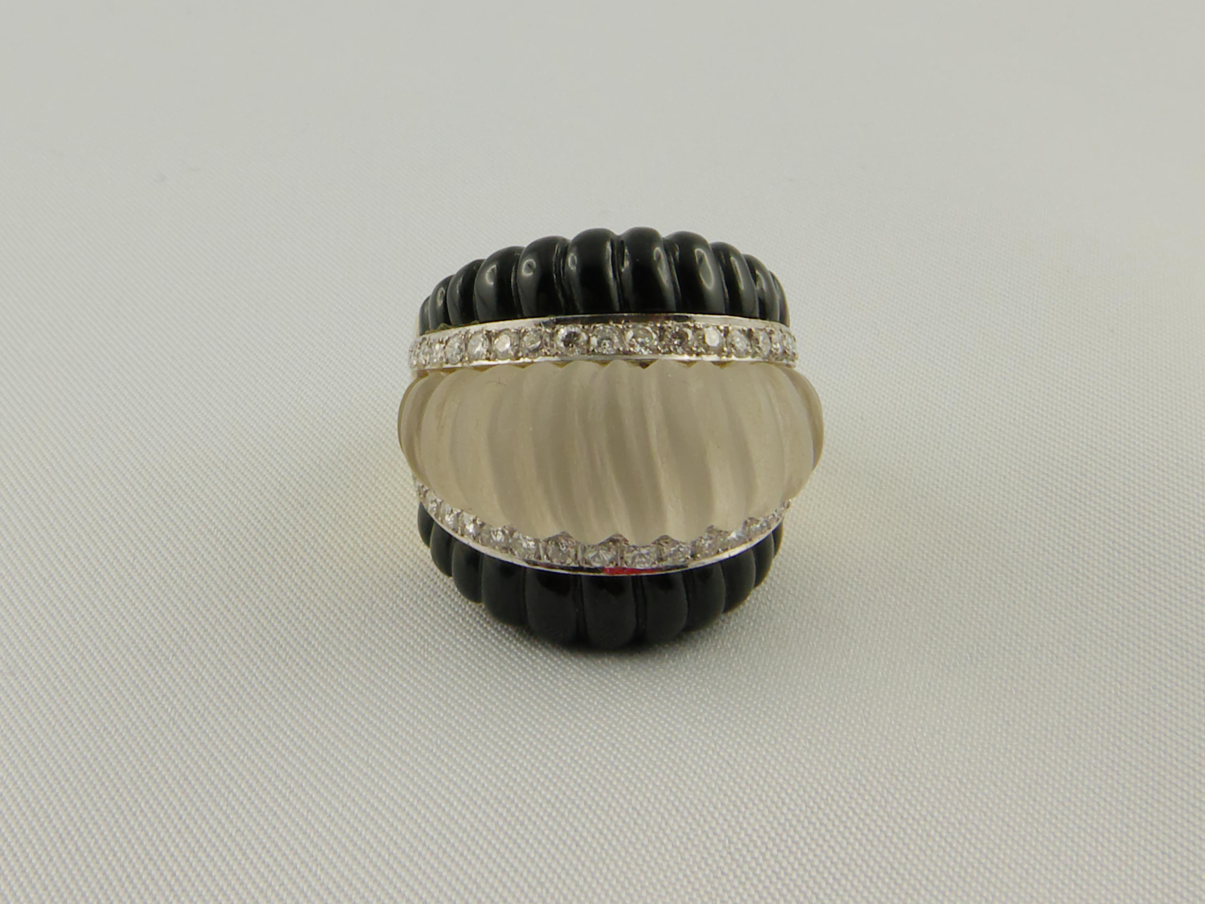 This sleek and  wearable 1970s ring is formed by two onyx layers alterned by a rock crystal layer, all of bombé  form,  fluted to create a wave motif.  
The ring is set in  yellow and white gold with  two horizontal strips of round-cut Diamonds