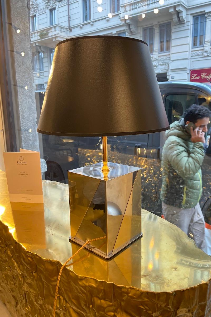 Lámpara de los años 70 de Romeo Rega. La base de la lámpara de mesa tiene forma rectangular, cada cara dividida oblicuamente con los dos materiales latón y acero. 
Su esencialidad lo hace versátil para cualquier entorno. La pantalla negra completa