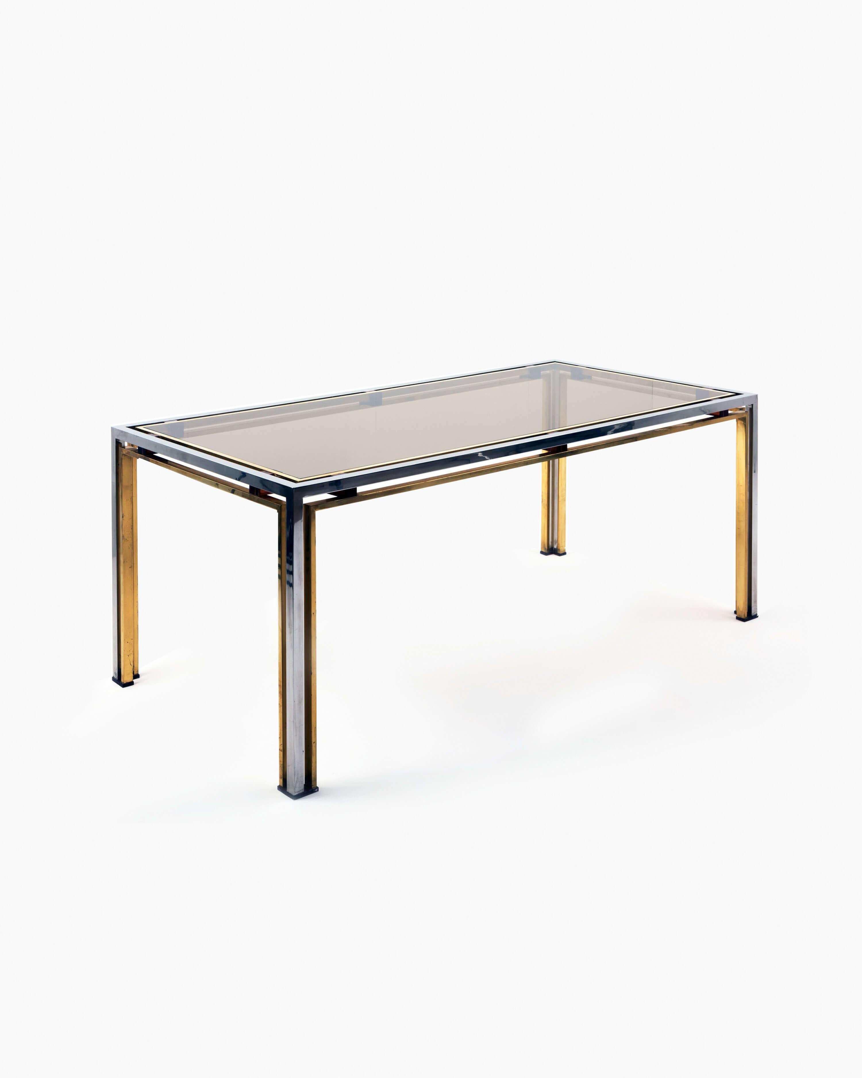 This rectangular dining table by Romeo Rega stands on four gilt and chromed brass legs, with a smoked glass top. Rega produced many entertainment-focussed pieces that have been favored by lovers of the Hollywood Regency. The reduced elegance of this