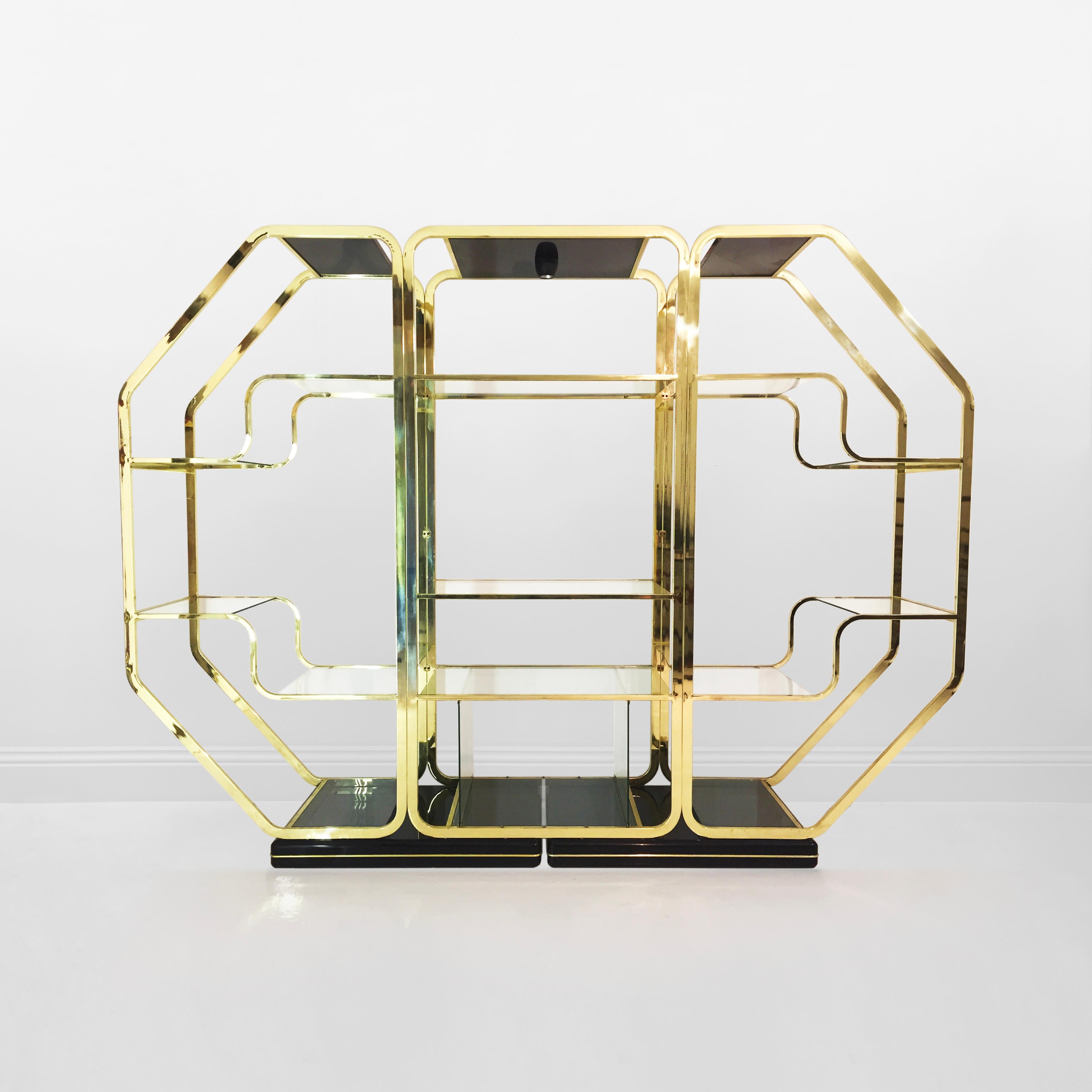 A 1970s Italian display unit in the manner of Romeo Rega or Renato Zevi, in a unique and large octagonal shape. The base is composed of two pieces of rectangular black lacquered wood, with curved edges and a brass trim. The piece is finished with a