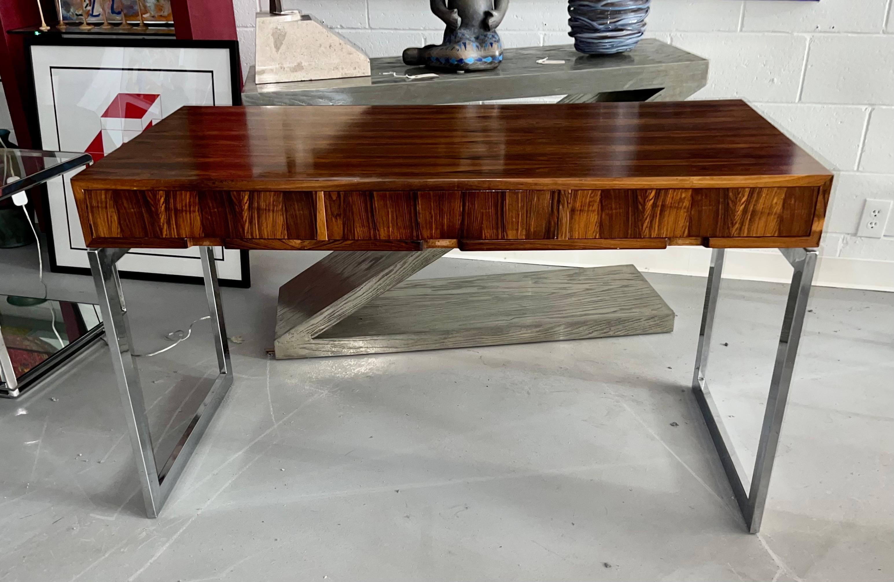A vintage 1970's three drawer rosewood veneered desk attributed to Milo Baughman. Nicely finished with solid wood interior drawers and chrome legs.Beautiful graining. In good age appropriate vintage condition with minor marks and imperfections. Some