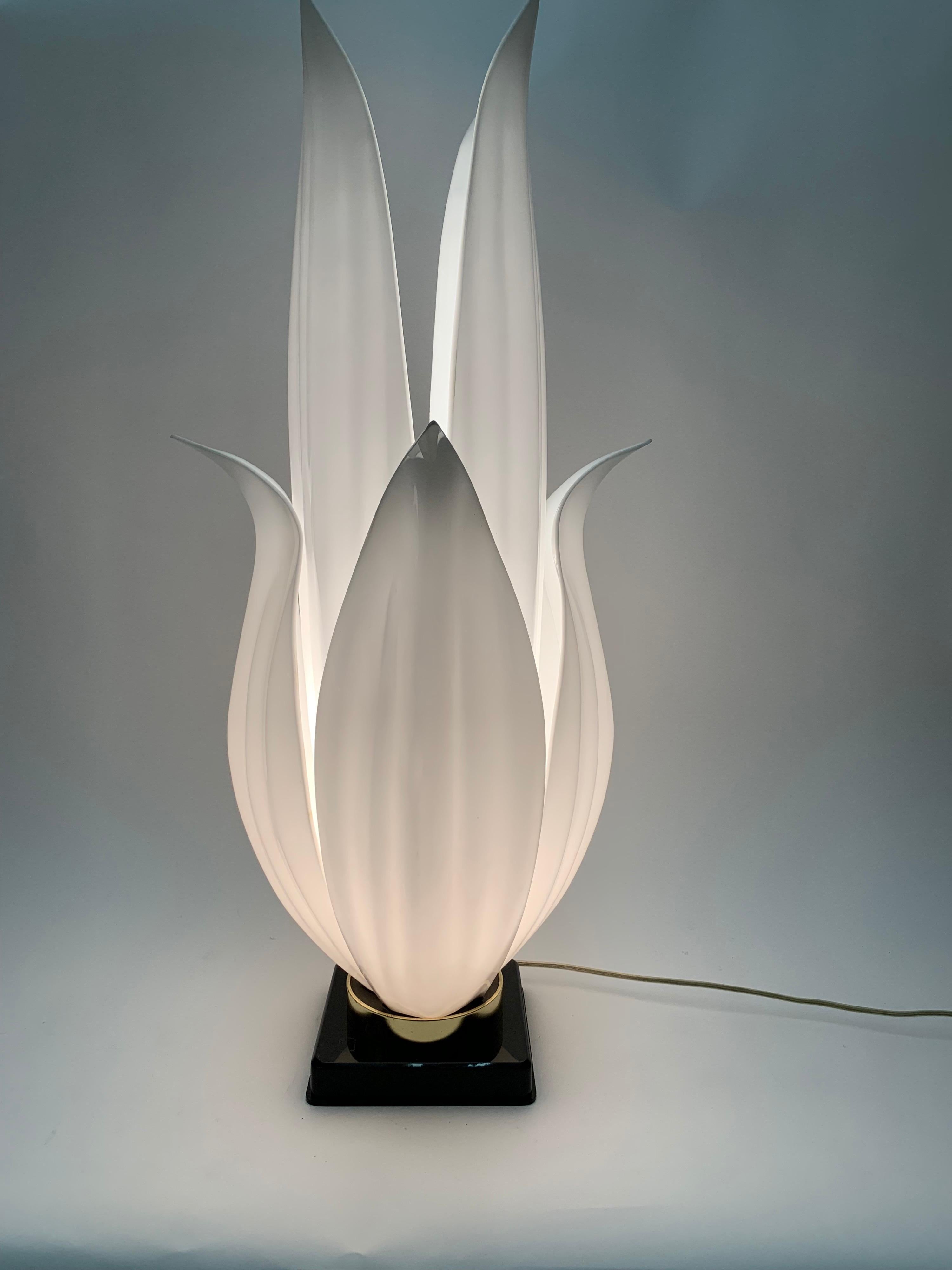 Large acrylic flower form lamp. This lamp is beautifully illuminated by a single bulb at the base. The petals are a white acrylic held together by a brass circle ring on top of a black square base.

Property from esteemed interior designer Juan