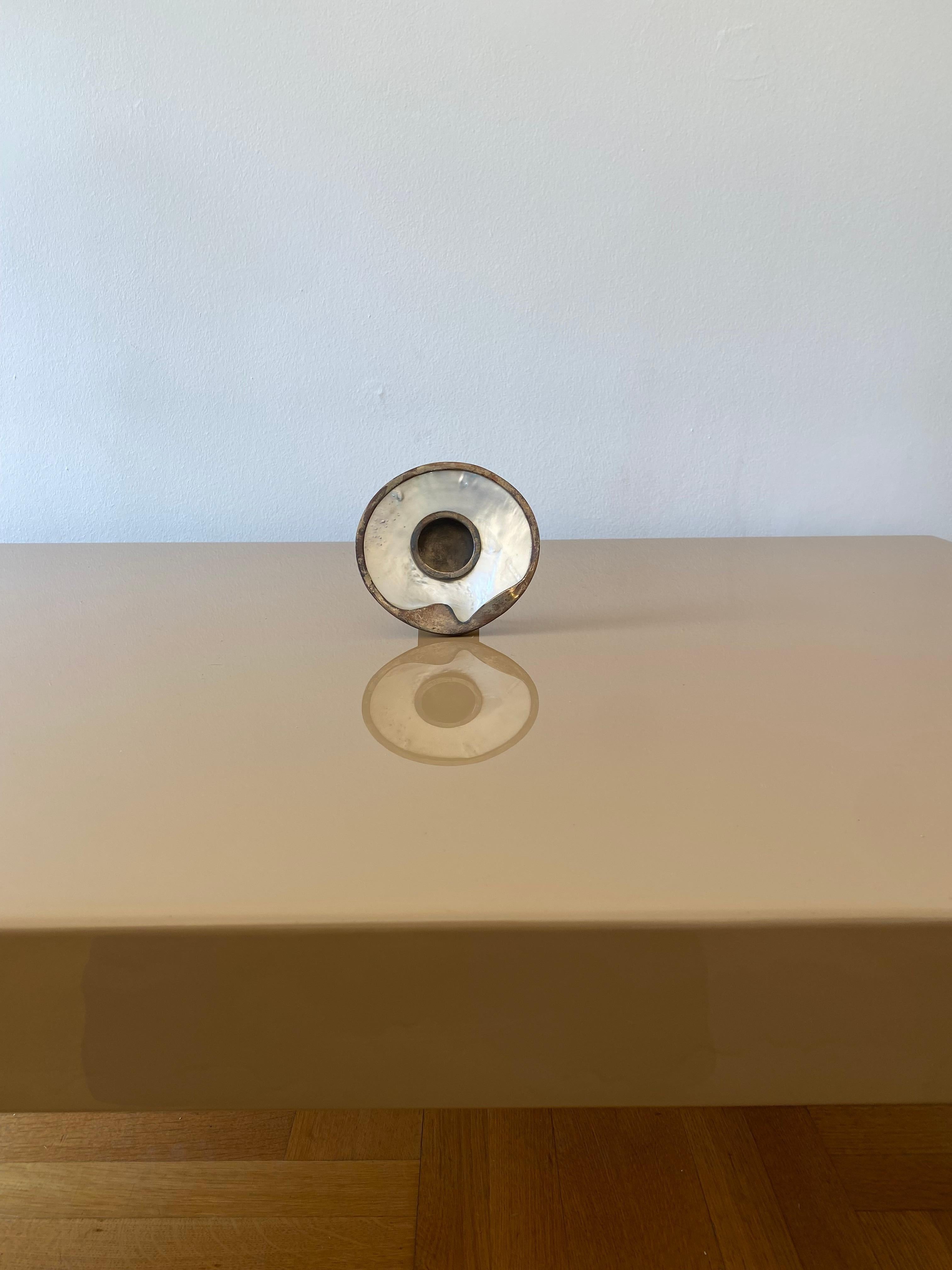 Un piccolo ma elegante portafoto in madreperla con finiture e supporto in argento.
Le finiture in argento seguono la forma rotonda in modo organico, con un inserto centrale sempre in argento per la fotografia che sostiene anche il supporto sul