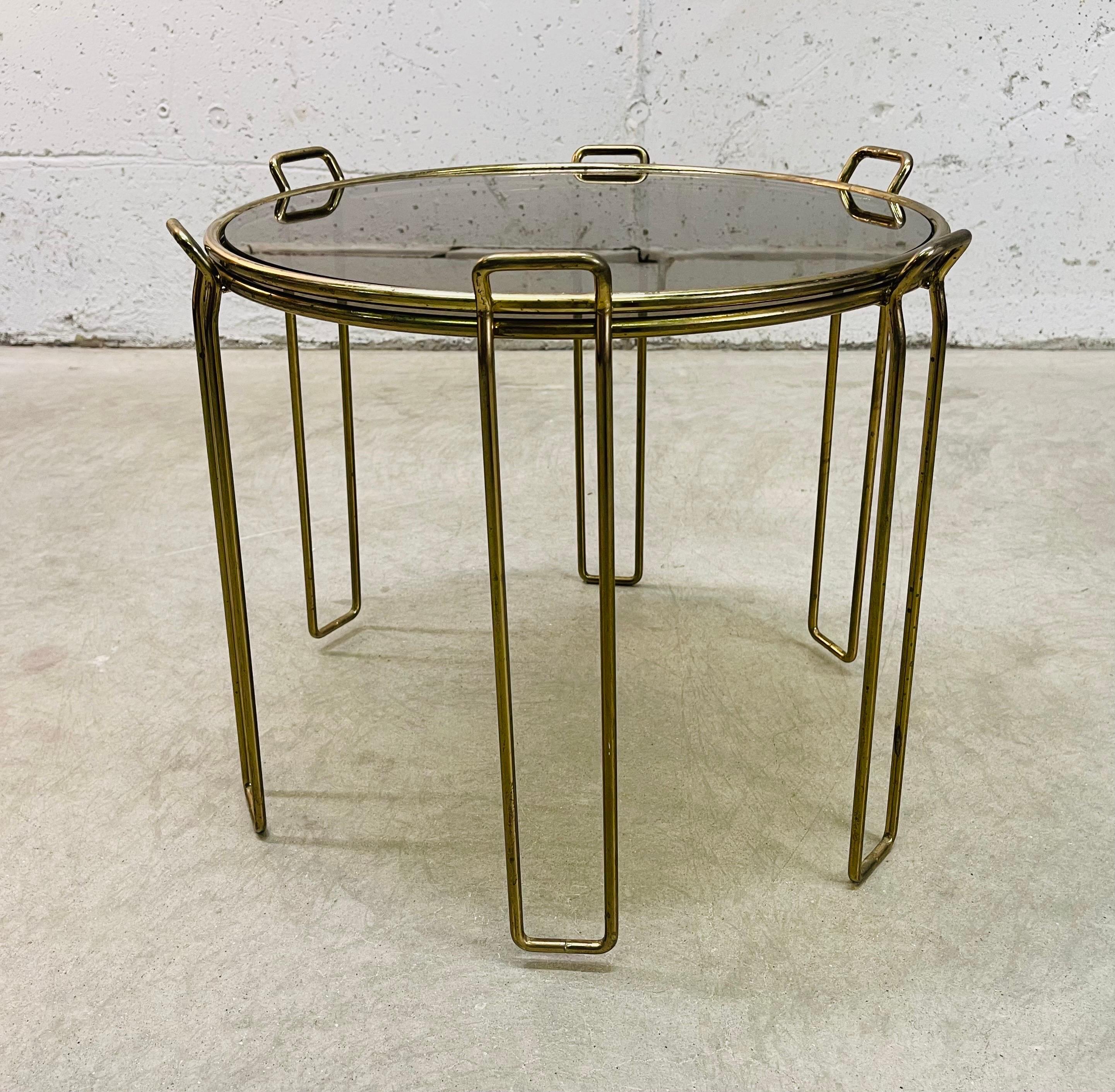 Vintage 1970s pair of round gold metal and smoked glass stacking side tables. Stack for easy storage. Both have light wear from use. Glass is in very good condition. No marks.