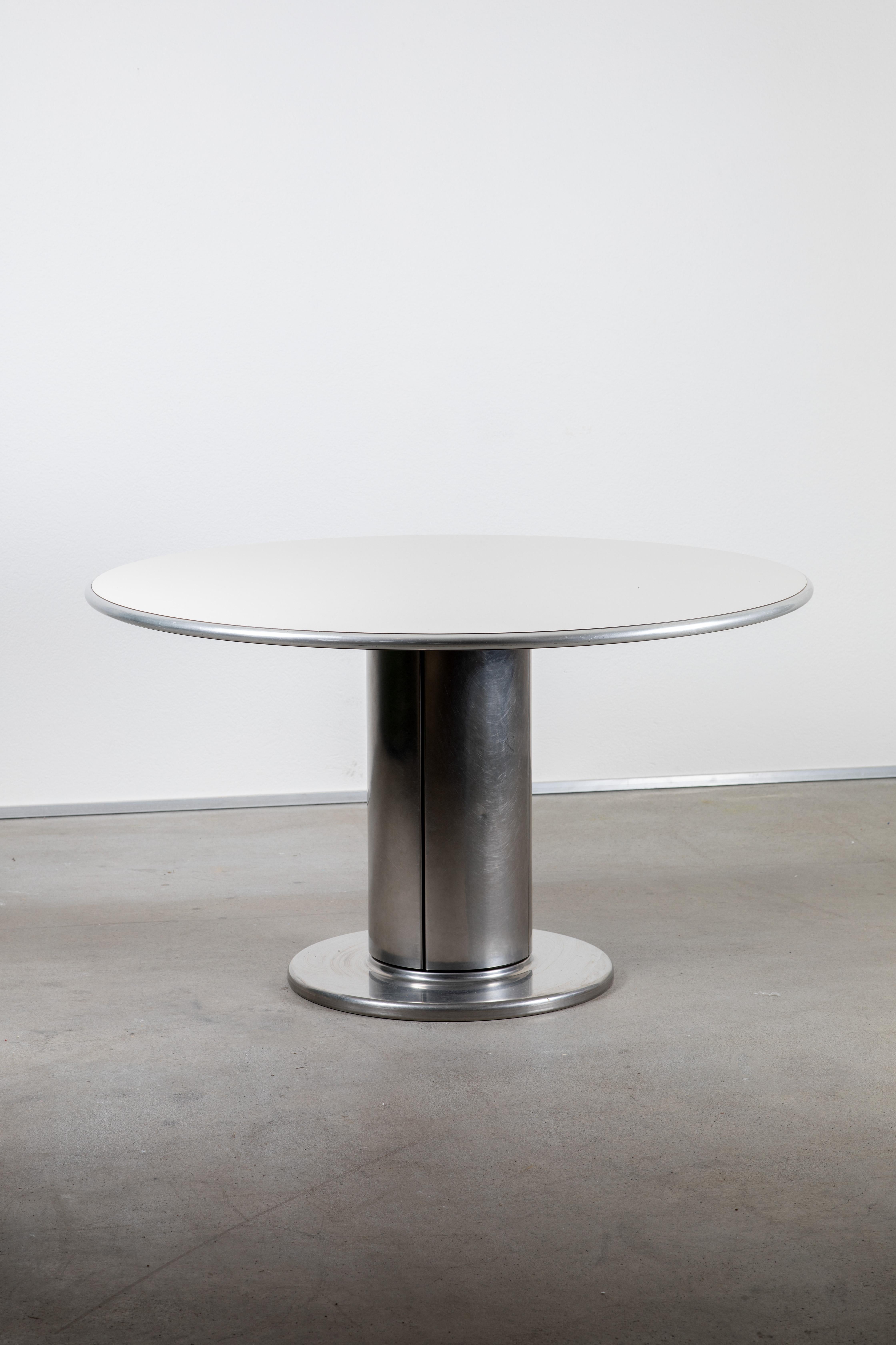 This statement midcentury round table boasts a sleek, cylindrical, chrome-plated base that exudes a strong sense of modernity and sophistication. The flat surfaces of the table are designed to reflect contemporary style, creating a bold and stylish