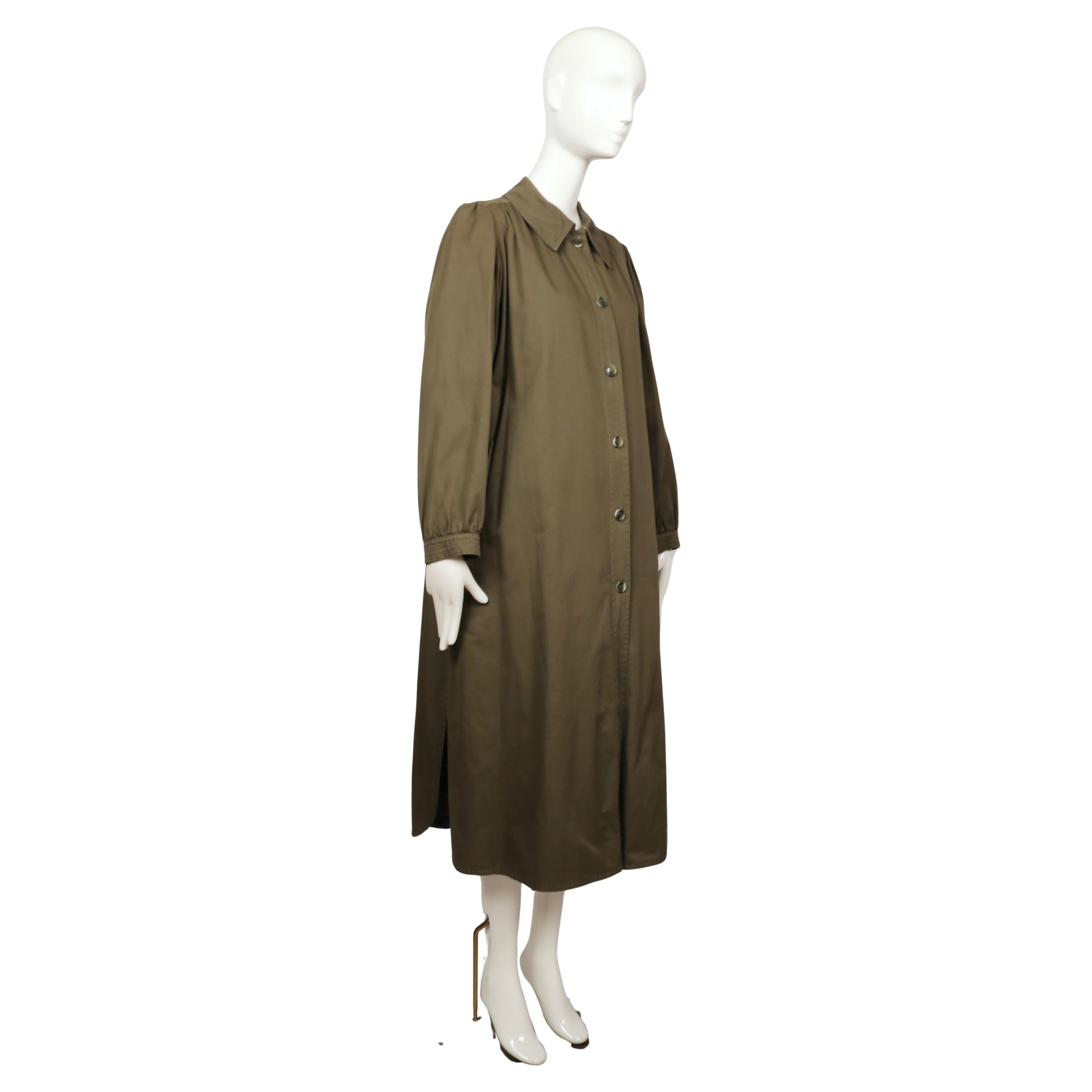 Raro trench Saint Laurent degli anni '70. Realizzato in gabardine di cotone color oliva intenso, presenta maniche a sbuffo morbidamente arricciate che aggiungono volume alla linea delle spalle, un classico colletto a punta e una silhouette dritta e