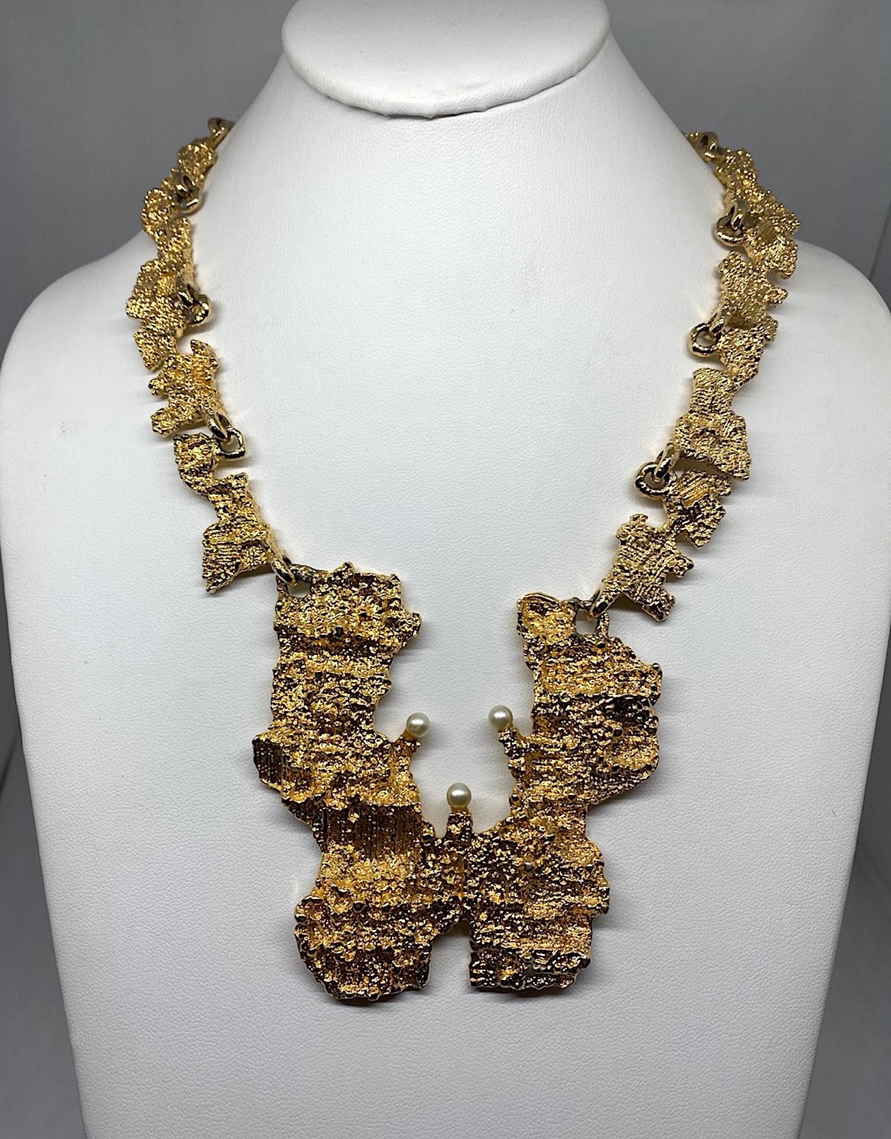 A wearable pieces sculpture is this 1970s brutalist gold plate necklace. The pendant and links are sculpted with a rough gold nugget texture in gold plate and accented with three faux pearls. The large pendant is 3.25 inches wide and 3.38 inches