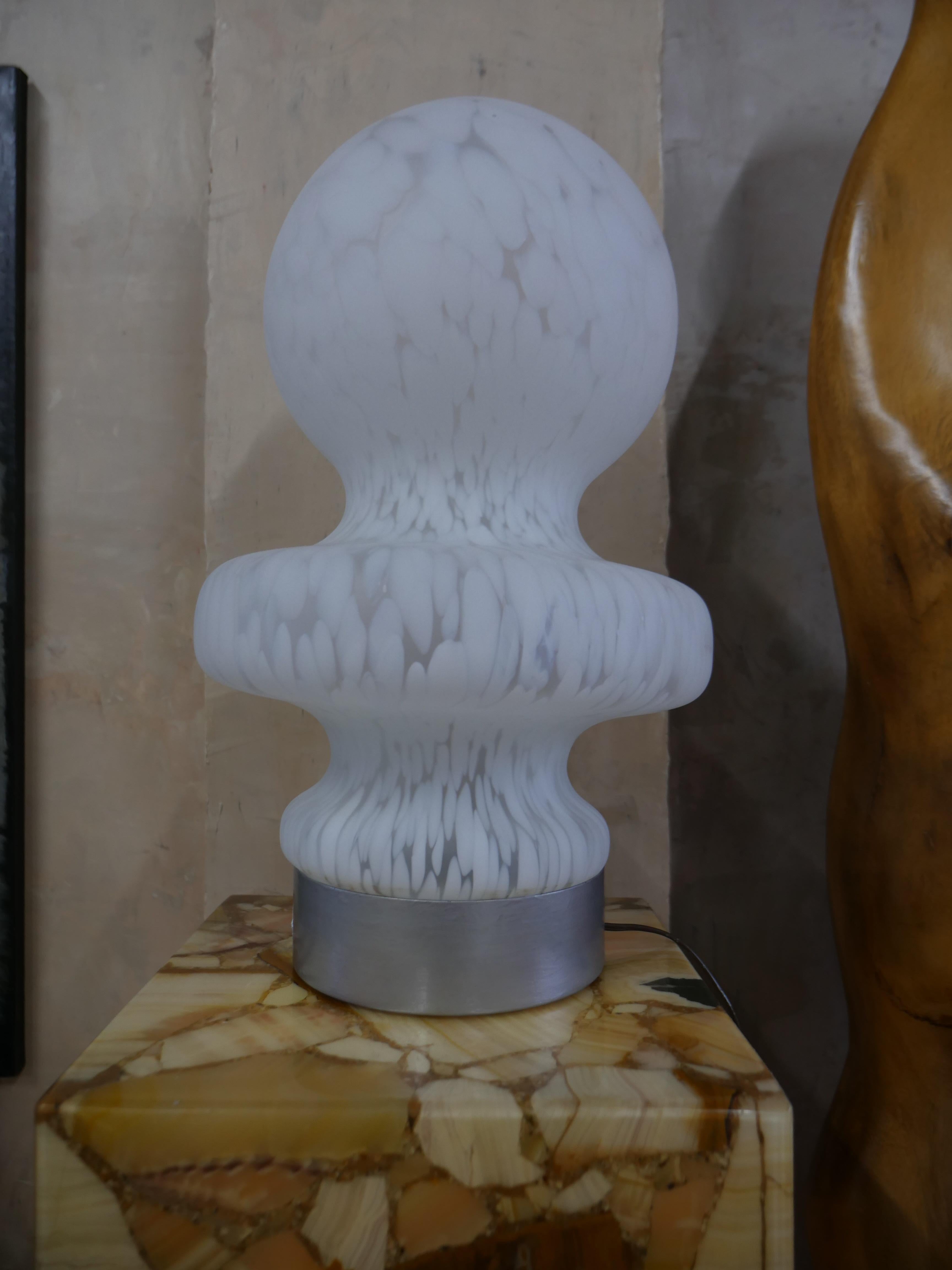 Preciosa lámpara de sobremesa de cristal soplado a mano que capta a la perfección la estética nostálgica de los años setenta. La lámpara está fabricada con cristal nublado texturizado, que emite un resplandor difuso que crea un ambiente cálido y