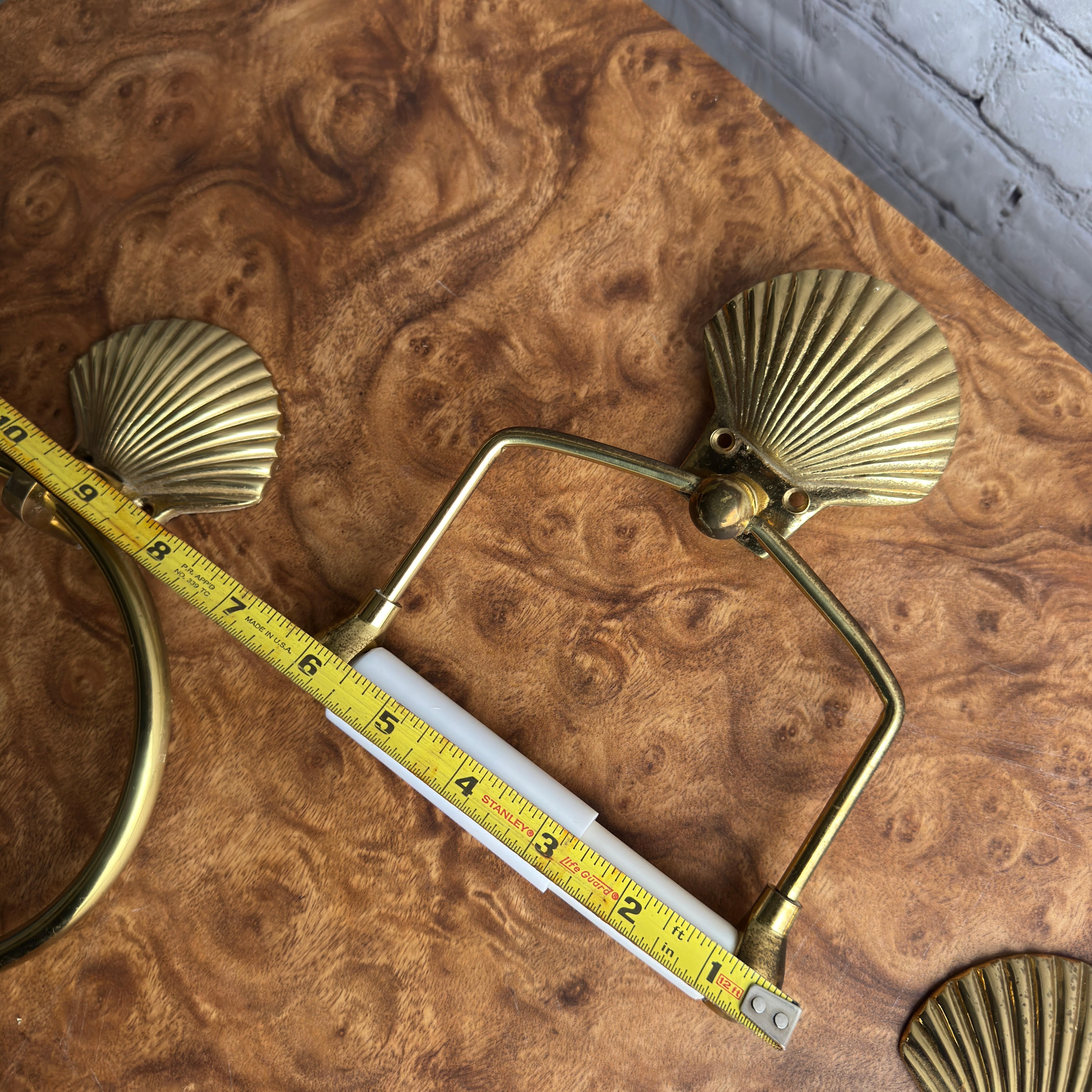 Pair of brass shell motif towel rings and a single brass toilet paper roll holder with a matching brass shell motif. They are all in very good shape. The toilet paper roll holder articulates 180 degrees so it will hold the many different toilet