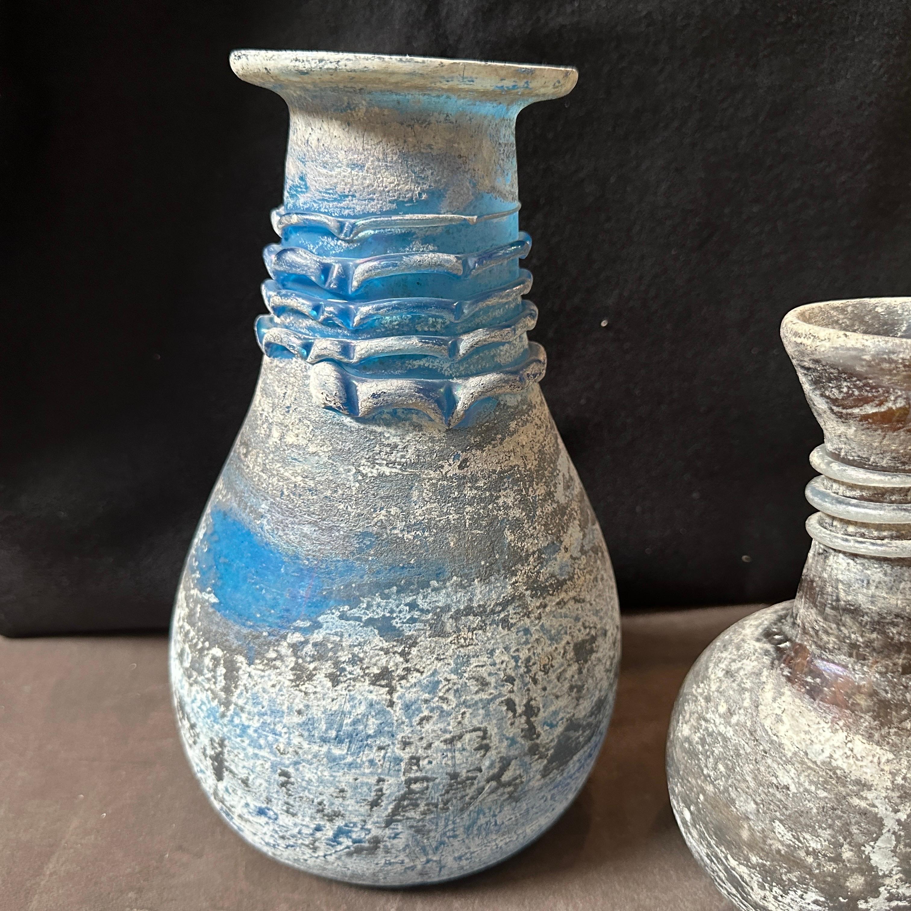 Due vasi in vetro di Murano Scavo realizzati a mano a Venezia negli anni Settanta. L'altezza dell'altro vaso è di 18 cm,  sono in ottime condizioni. Il vetro scavo è un tipo di vetro che ha un aspetto intenzionalmente invecchiato o rovinato dagli