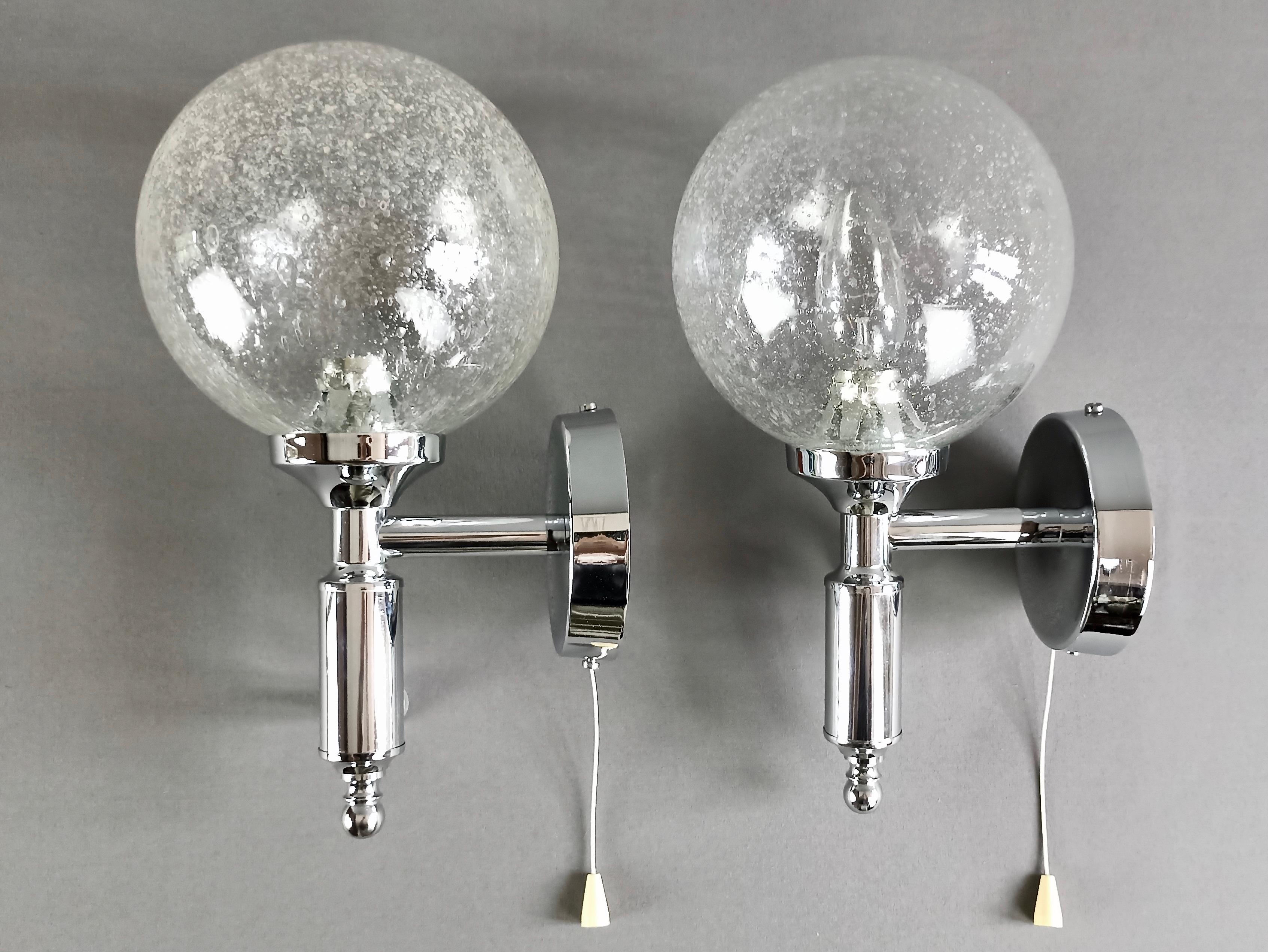 Beautiful pair of wall lamps from the 1970s, in chrome-plated metal and spherical Murano glass shades with Pulegoso work.
This particular type of glass, called 'Pulegoso' in Murano glassworks, is characterised by innumerable tiny, irregular air
