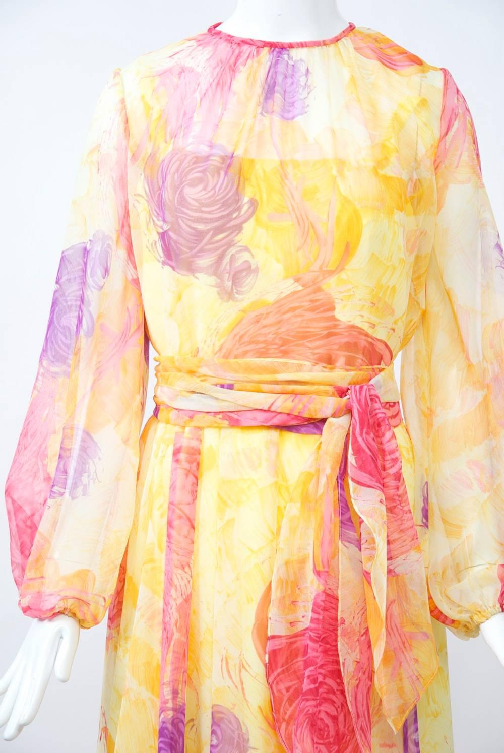 Sheer print gown by Robert Courtney of yellow background with impressionistic watercolor flowers in purple, red, yellow, orange. Style features shirred jewel neckline, long balloon sleeves, and a softly falling skirt. A large sash is the finishing