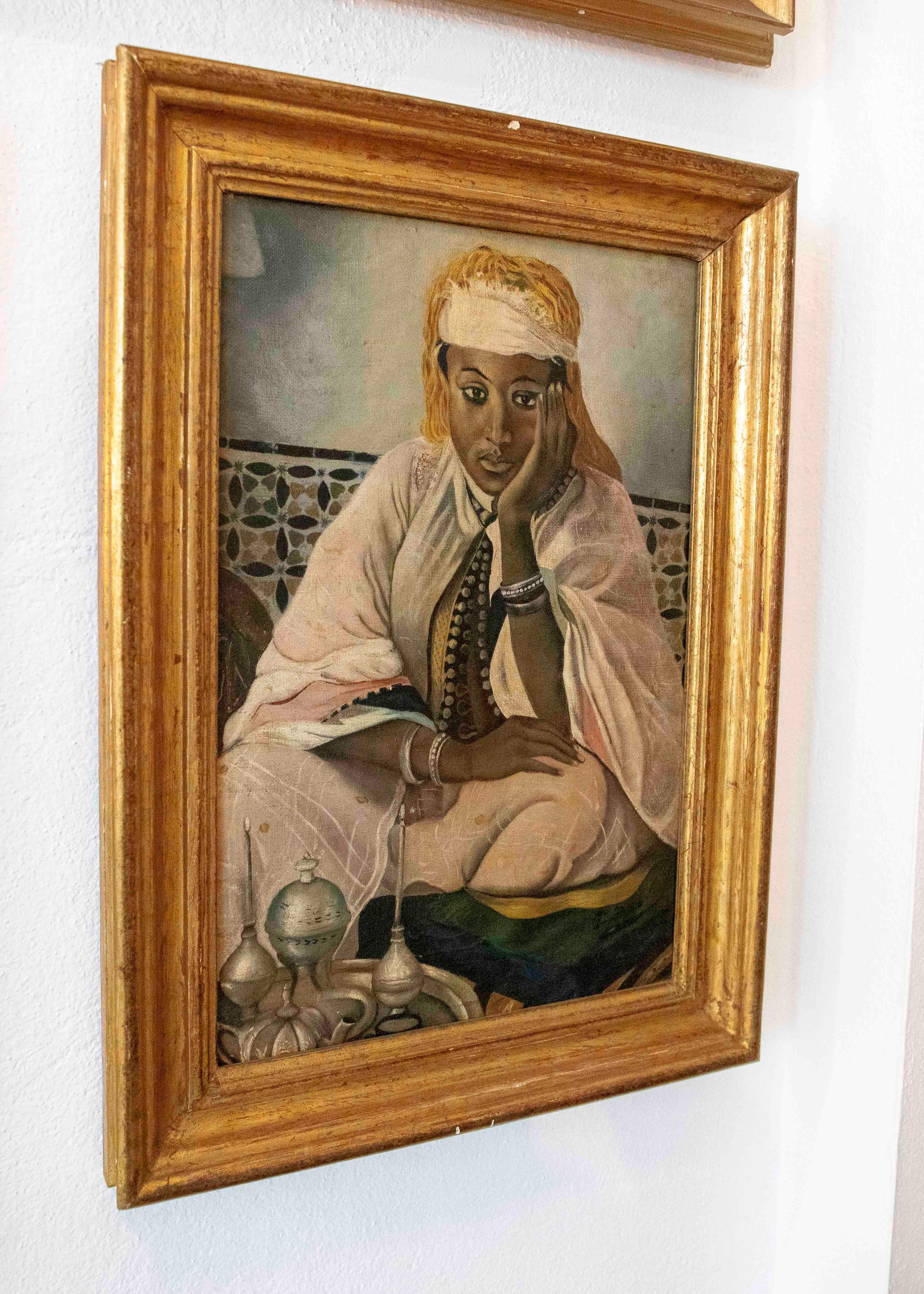 Olio su tela incorniciato da una modanatura dorata che raffigura una donna etiope seduta in un ambiente interno con uno sfondo geometrico. La figura è vestita con abiti tradizionali e posa serenamente, appoggiando il viso su una mano.

In primo