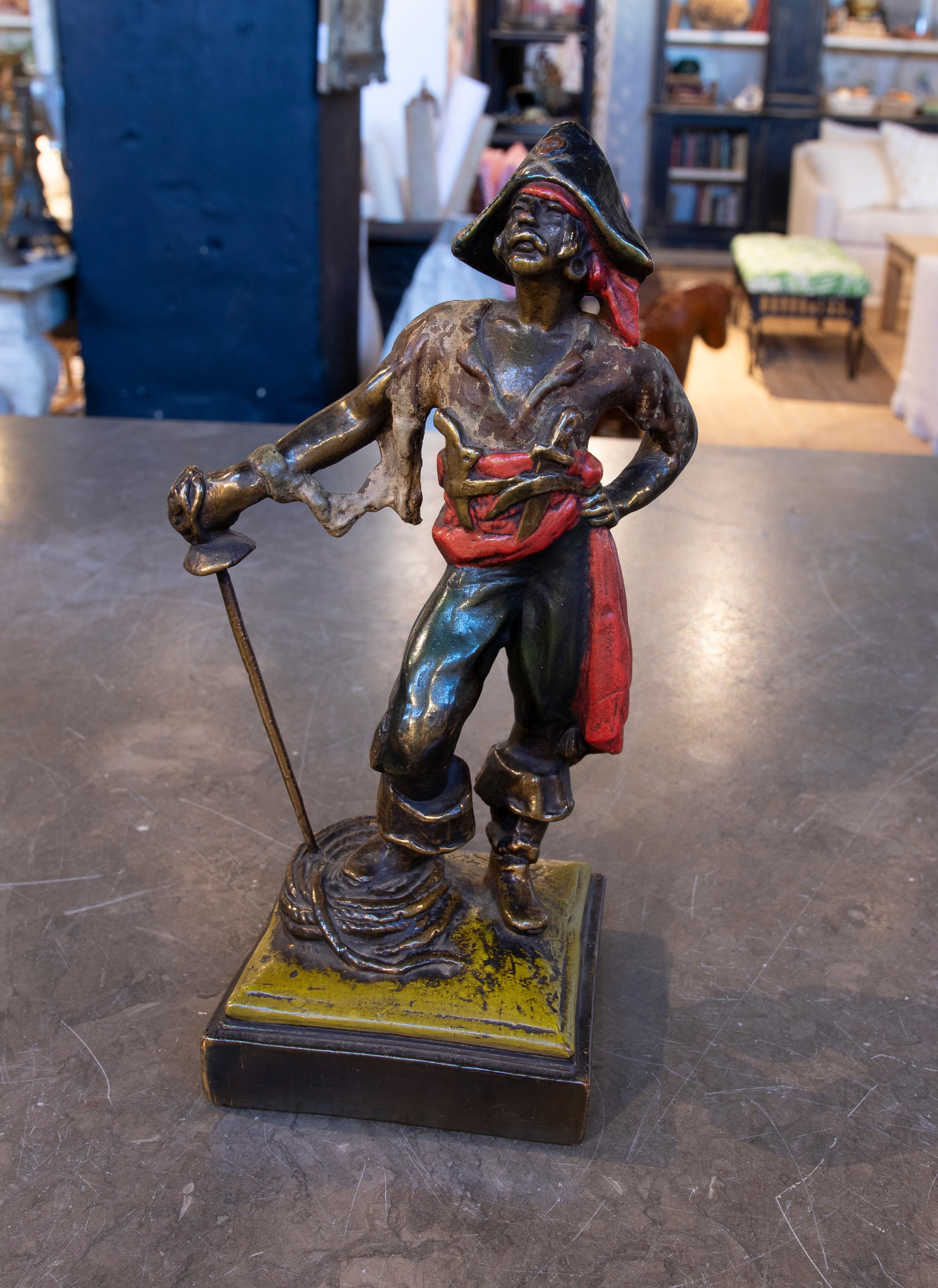 Bronze figure depicting a pirate in a defiant stance, sword in hand and imposing expression. His detailed attire, complete with a red scarf and signature tricorn hat, highlights the character's adventurous spirit. The base of the sculpture includes