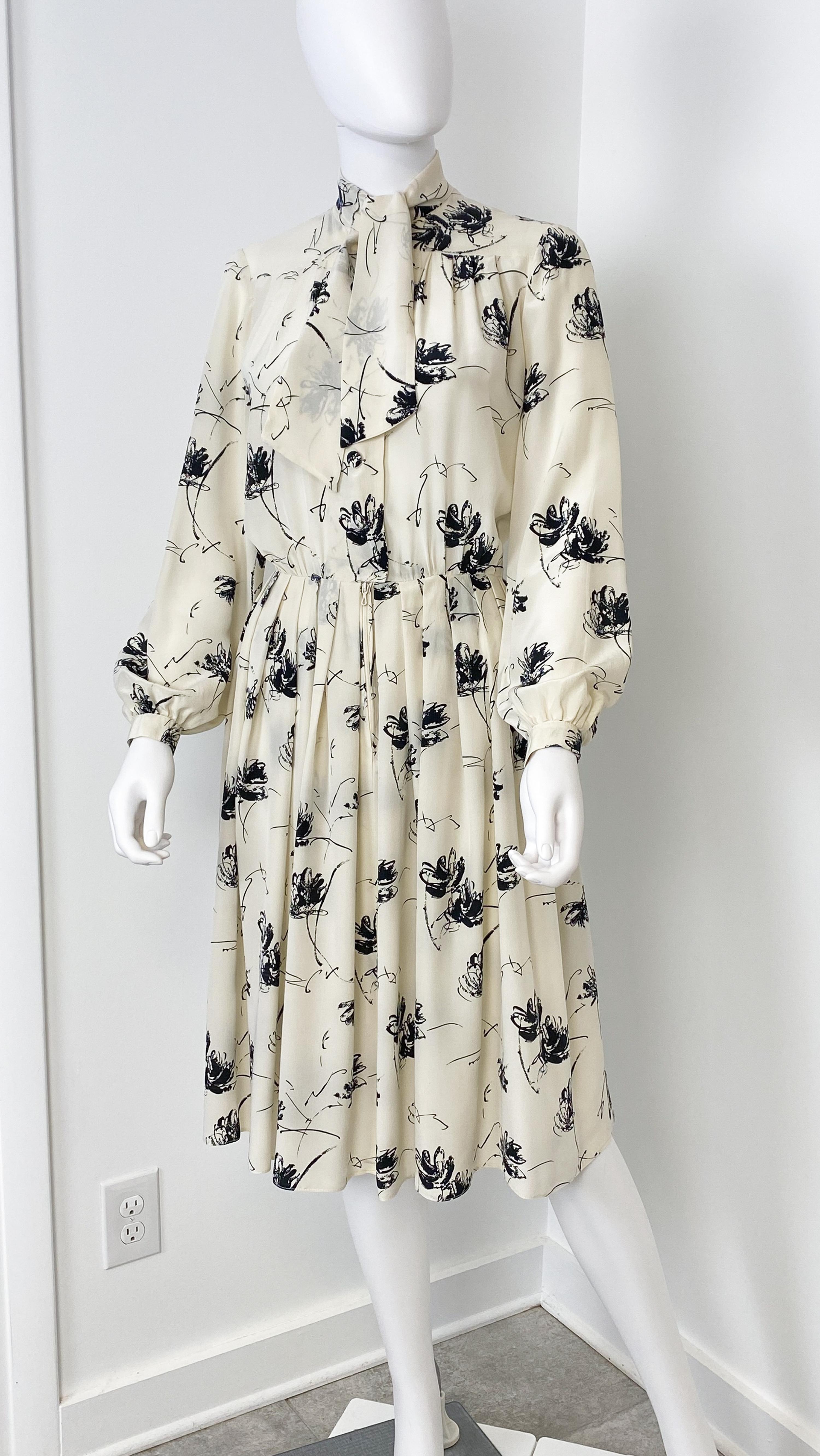 This exquisite vintage 1970s cocktail dress captures the era’s signature elegance with its flowing silhouette, full swirling skirt, and graceful long sleeves. Crafted from silk mousseline in a luminous cream-white hue, its slightly sheer fabric is