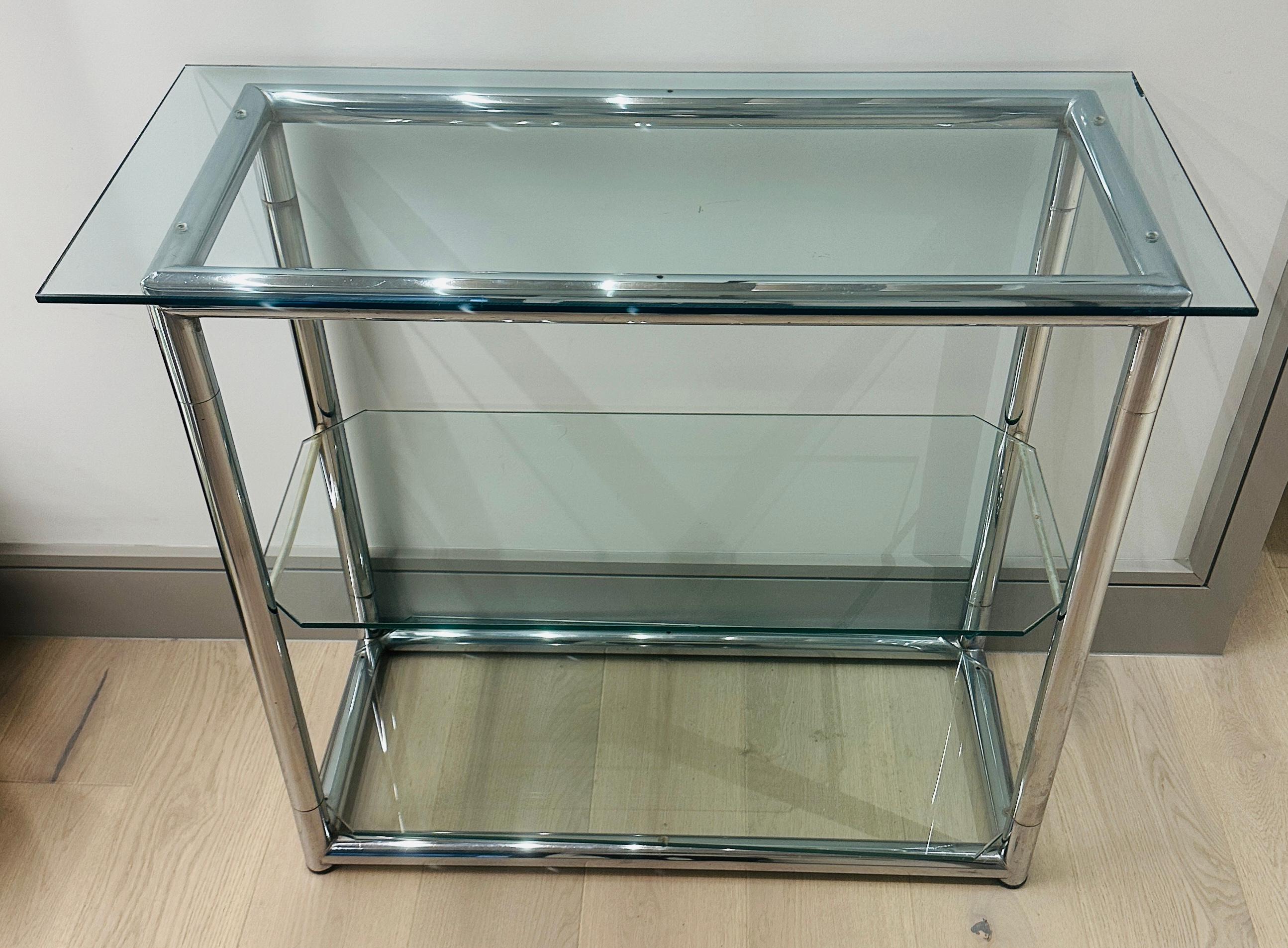 Pequeña estantería de tres baldas de metal cromado y cristal de la Bélgica de los años 70, perfecta para un espacio pequeño, como un pasillo o debajo de una escalera.  Los estantes central e inferior tienen esquinas biseladas que permiten
