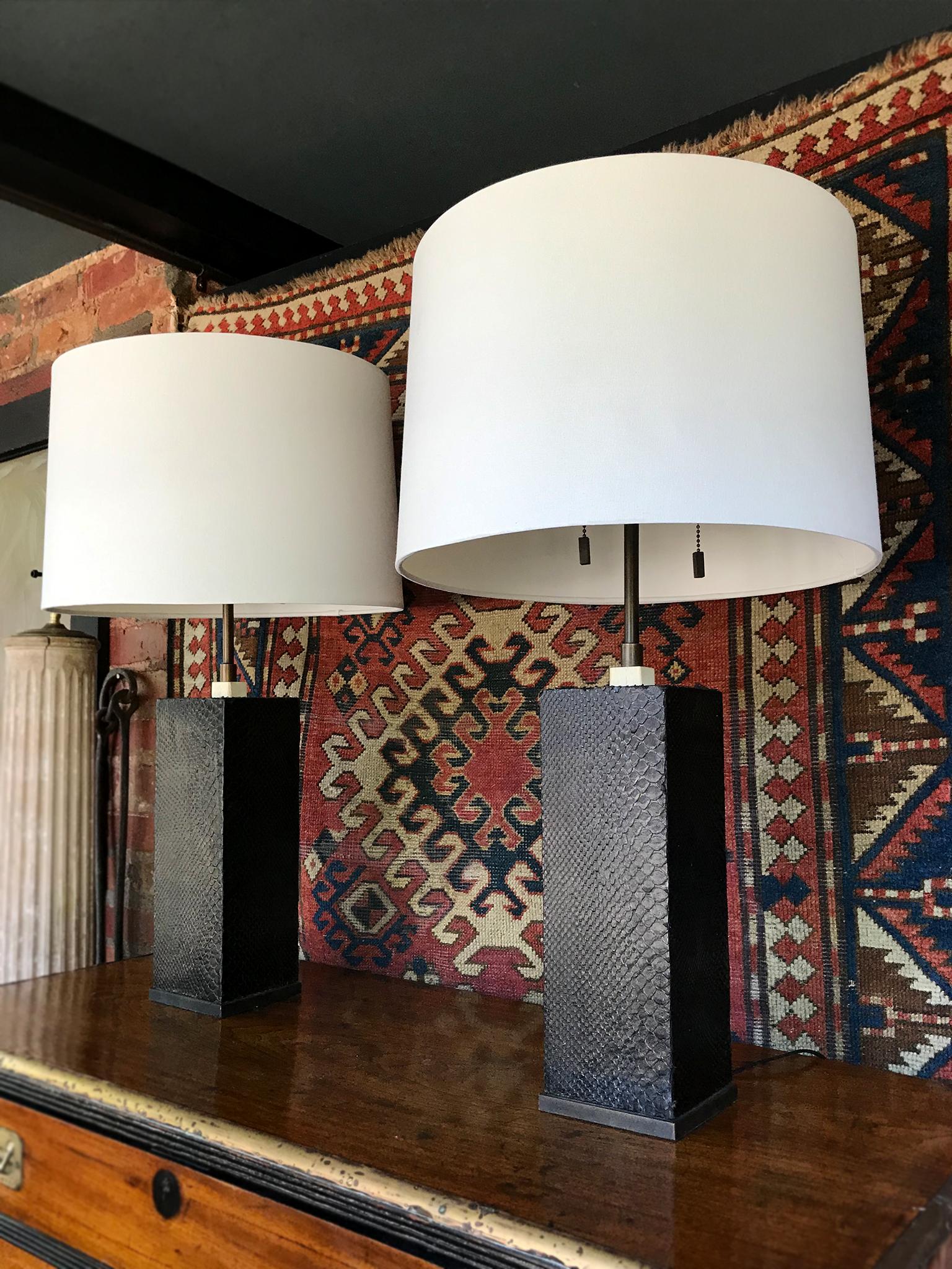 An elegant pair of column table lamps wrapped with a metallic-black snakeskin. Made in the 1970s. They are in the style of Karl Springer, who used unconventional materials to add texture and pattern to his Minimalist designs. The lamps are