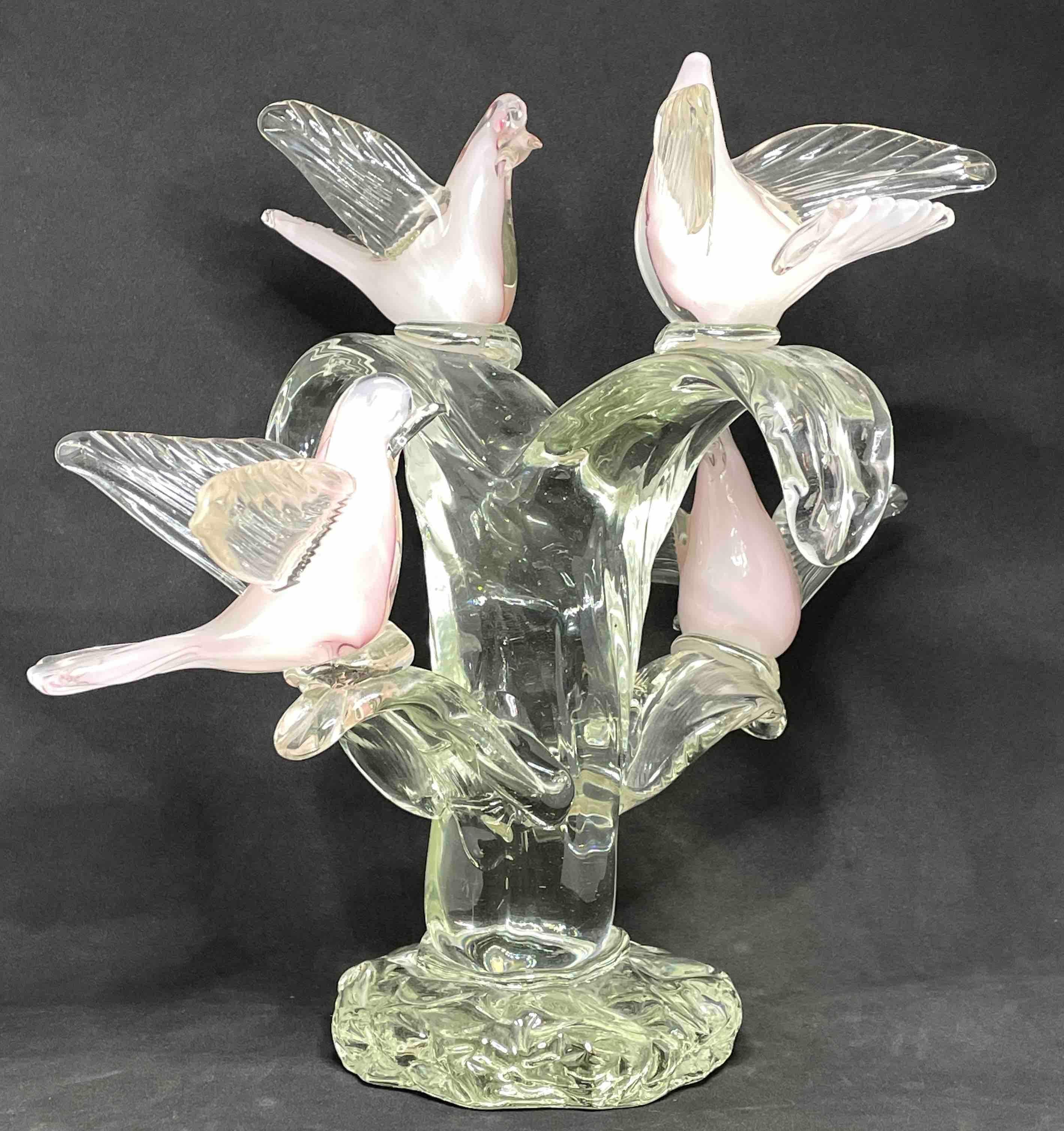 A Murano glass sculpture depicting four birds in white and light pink perched on a clear glass tree with branches attached to a base decorated with rounds. A nice centerpiece in each room. 