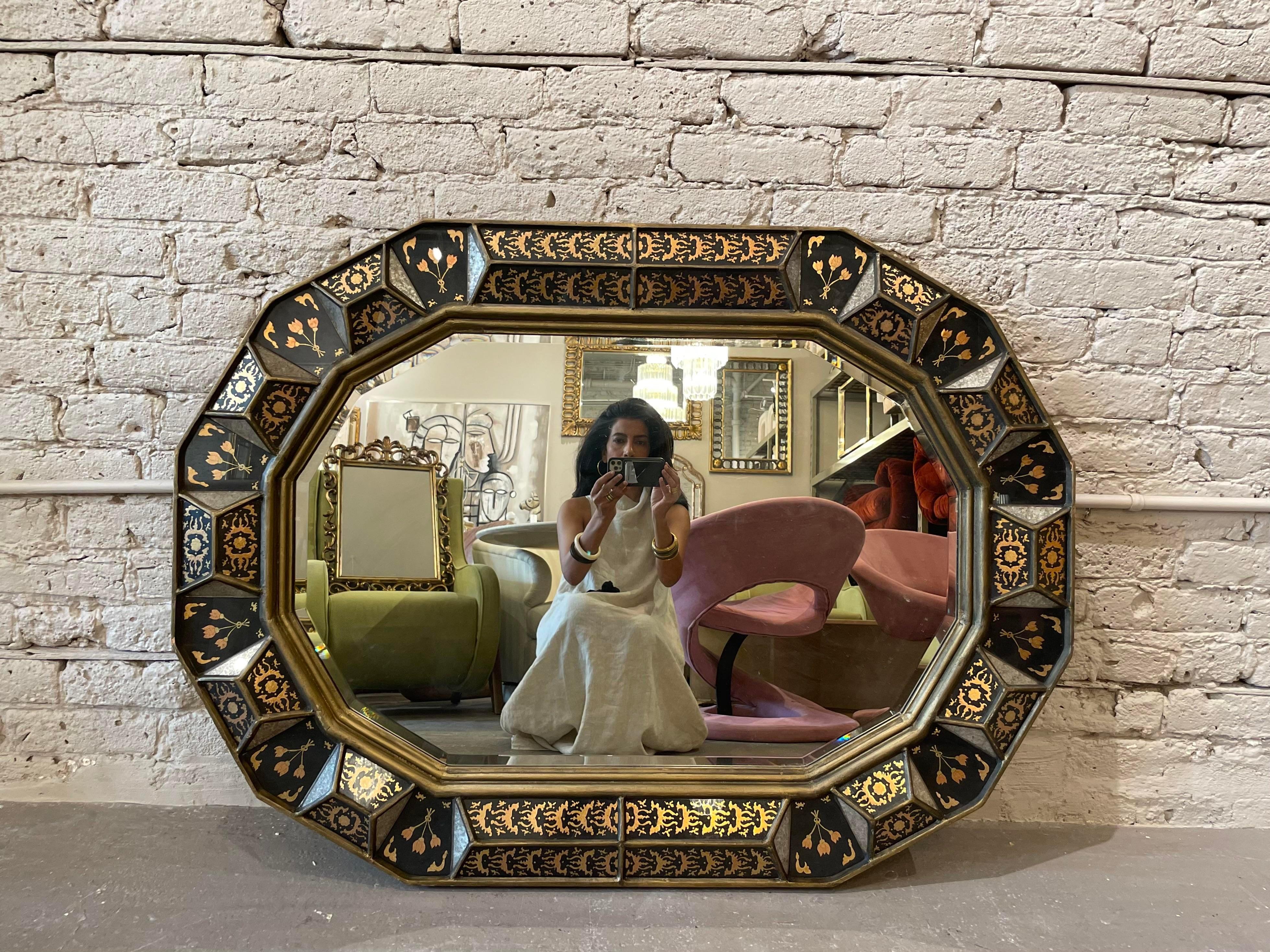 This stunning 12 sided eglomise style mirror from Baker Furniture has a geometric and dimensional frame. Gold trim, black panels, and gold details give boldness to the opulent design. The back has a label plaque marked “Baker / Furniture” and