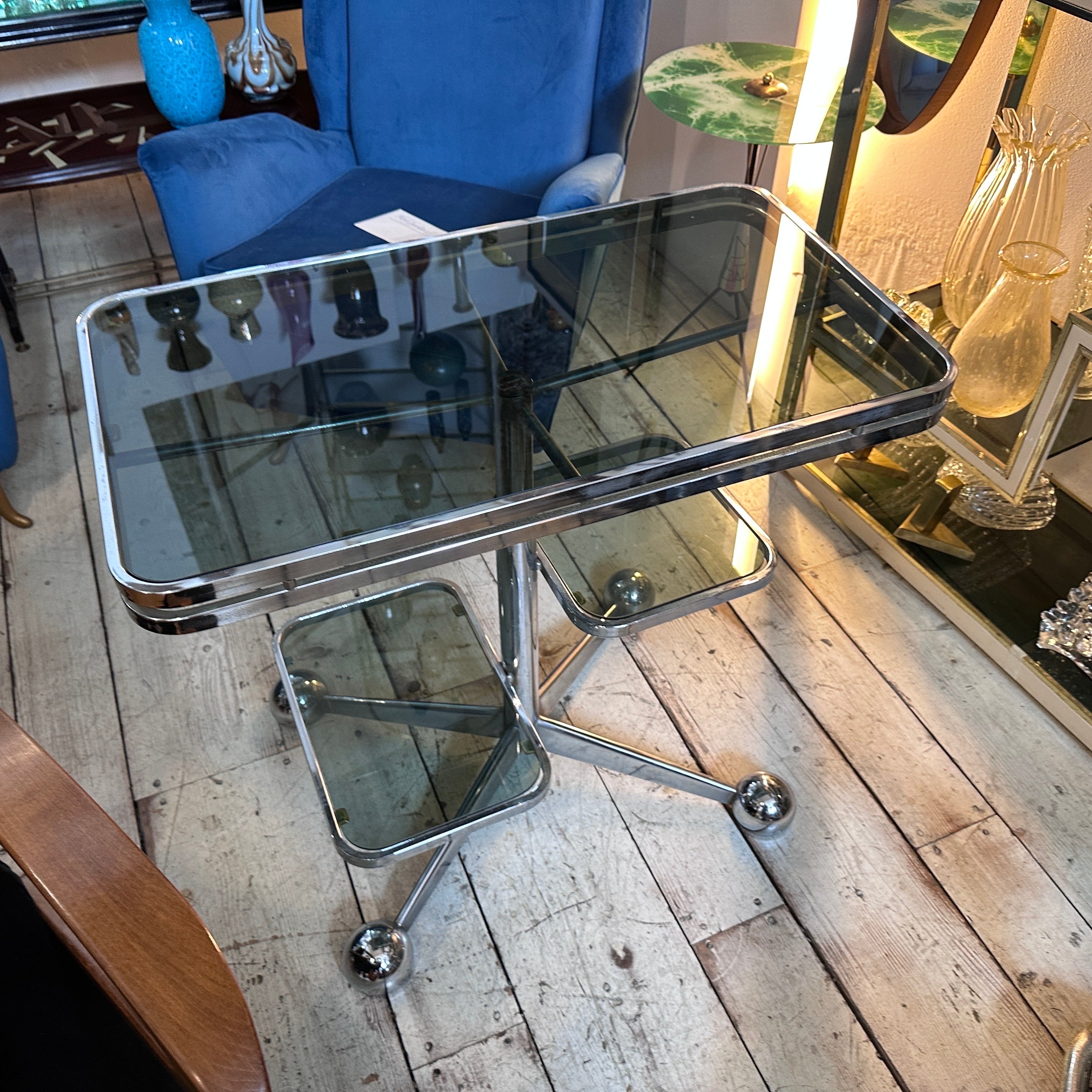 A muti-level bar cart designed and manufactured in the Space Age era by Allegri Arredamenti, the chromed metal and the dark glasses are in good conditions, it's labeled on the central foot. The 1970s Space Age design movement was characterized by