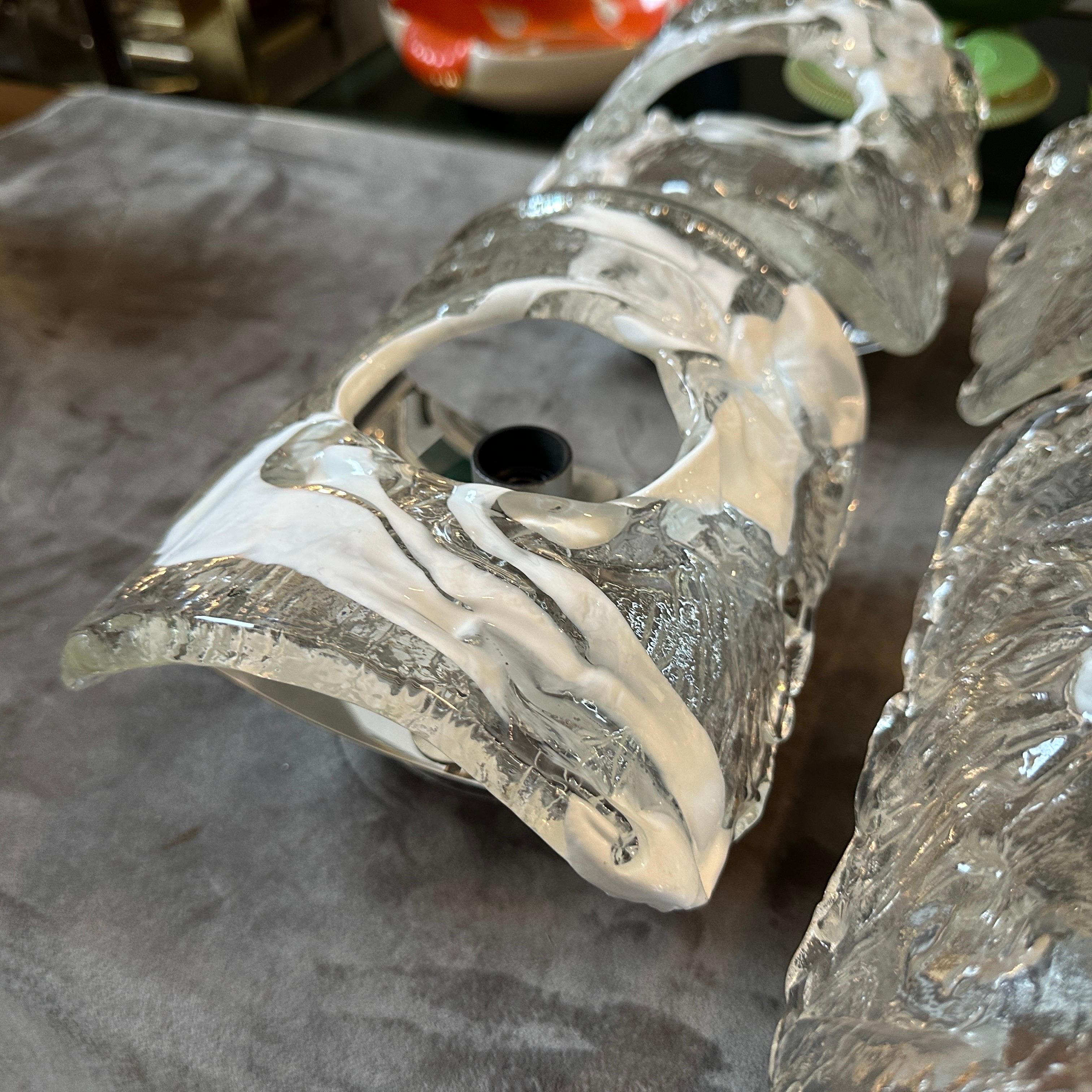 These wall sconces designed in the 1970s Space Age style by Mazzega are in working order and in perfect conditions. These fixtures feature a combination of clear and white Murano glass with a central steel element. The design showcases the signature