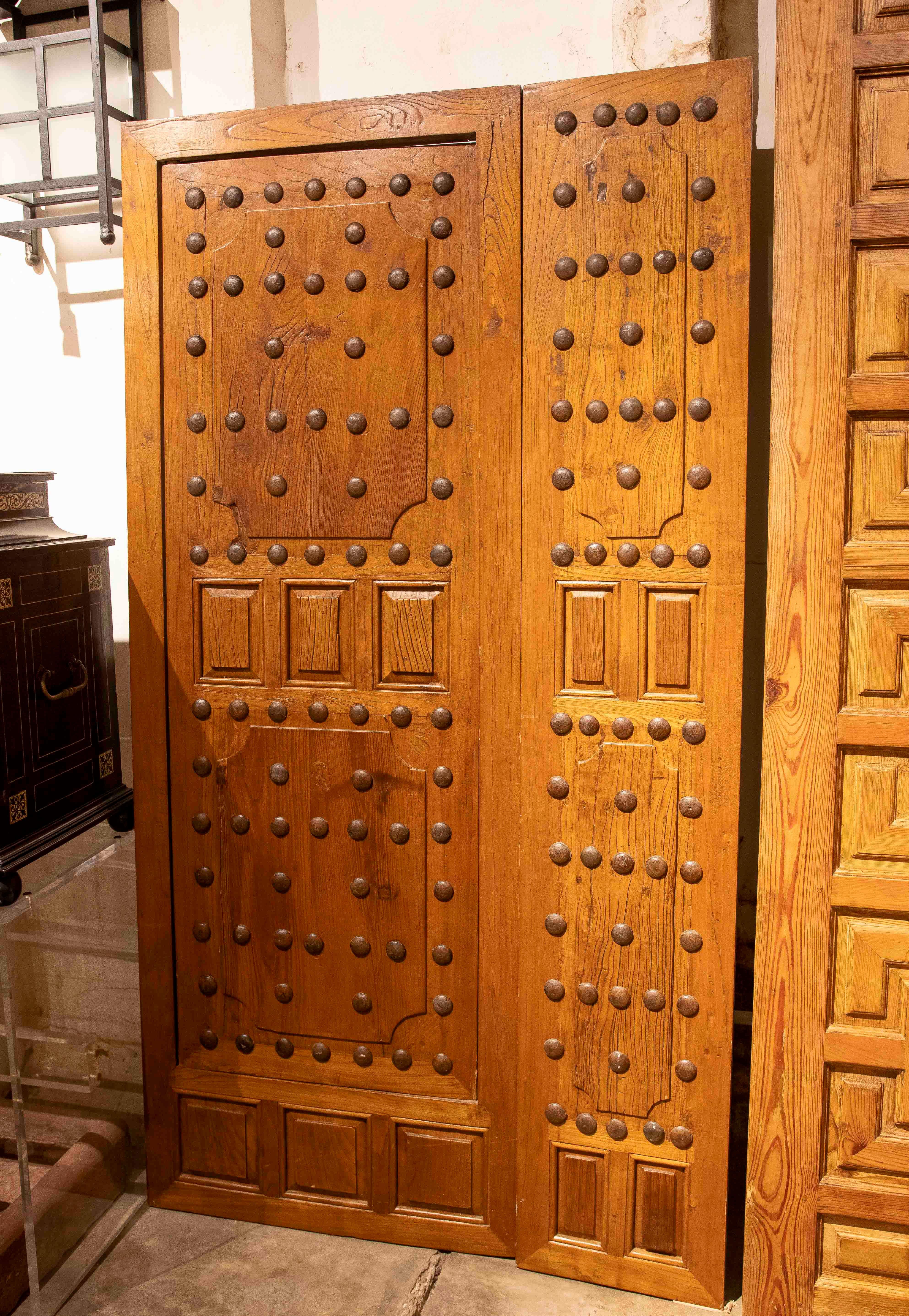 This stunning set of solid wood double doors features a traditional Castilian design, accentuated by large forged studs that decorate their surfaces. Their sturdy structure and symmetrical stud arrangement evoke historic Spanish architecture, making