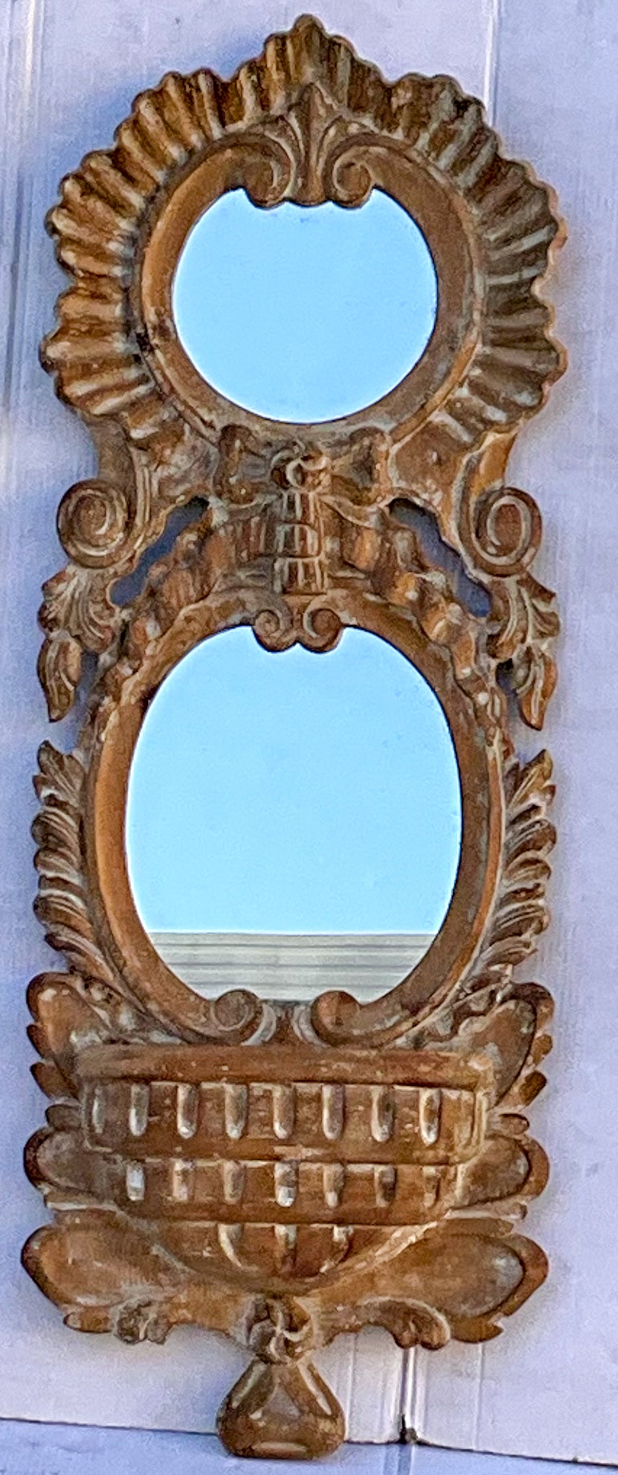 This is a heavily carved dual mirror with basket form wall pocket. It is unmarked but could possibly be by Sarreid.