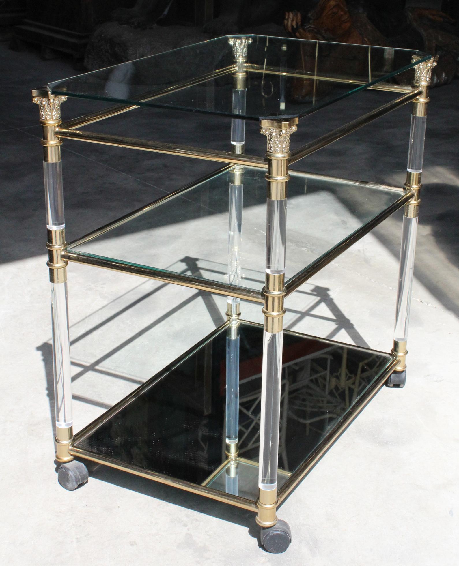 1970s Spanish methacrylate and glass TV table with brass bars and Corinthian capitals. It has wheels and a mirror on the bottom shelf.