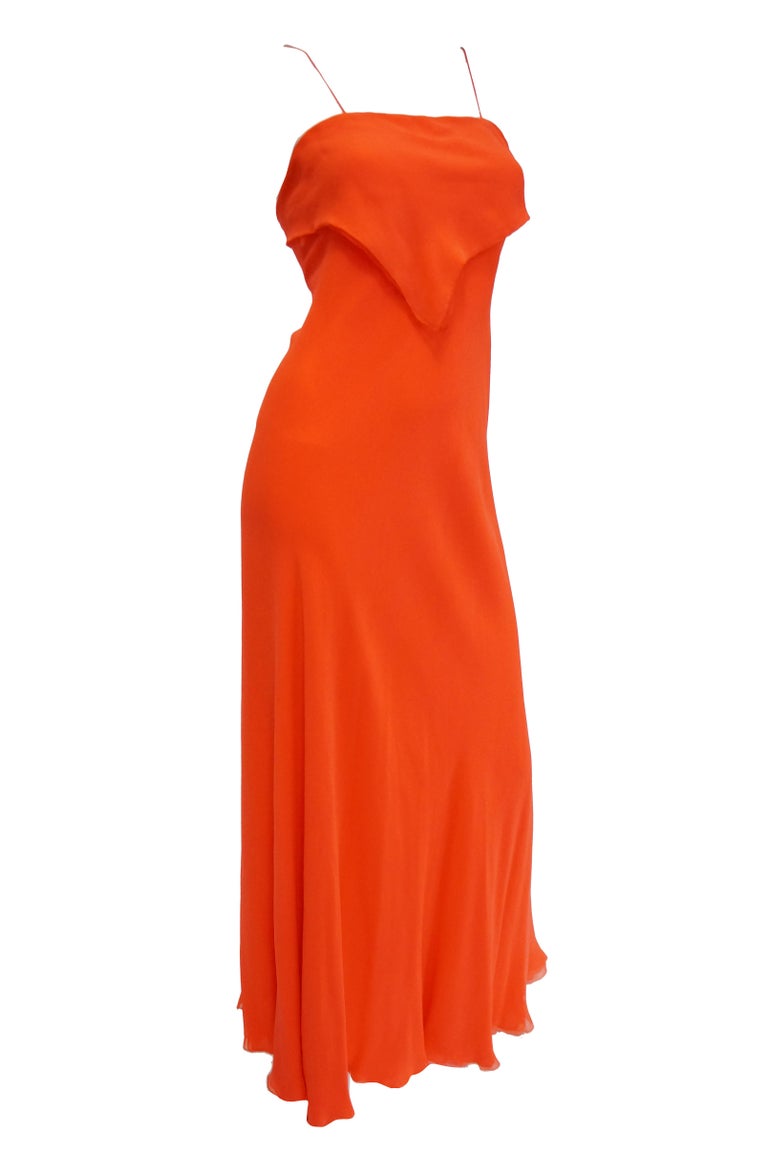 Astounding neon red evening dress ensemble consisting of a dress and long coat by George Stavropoulos! The red dress is maxi length, with spaghetti straps and a columnar silhouette. The dress features a thin, triangular, double layer of fabric that