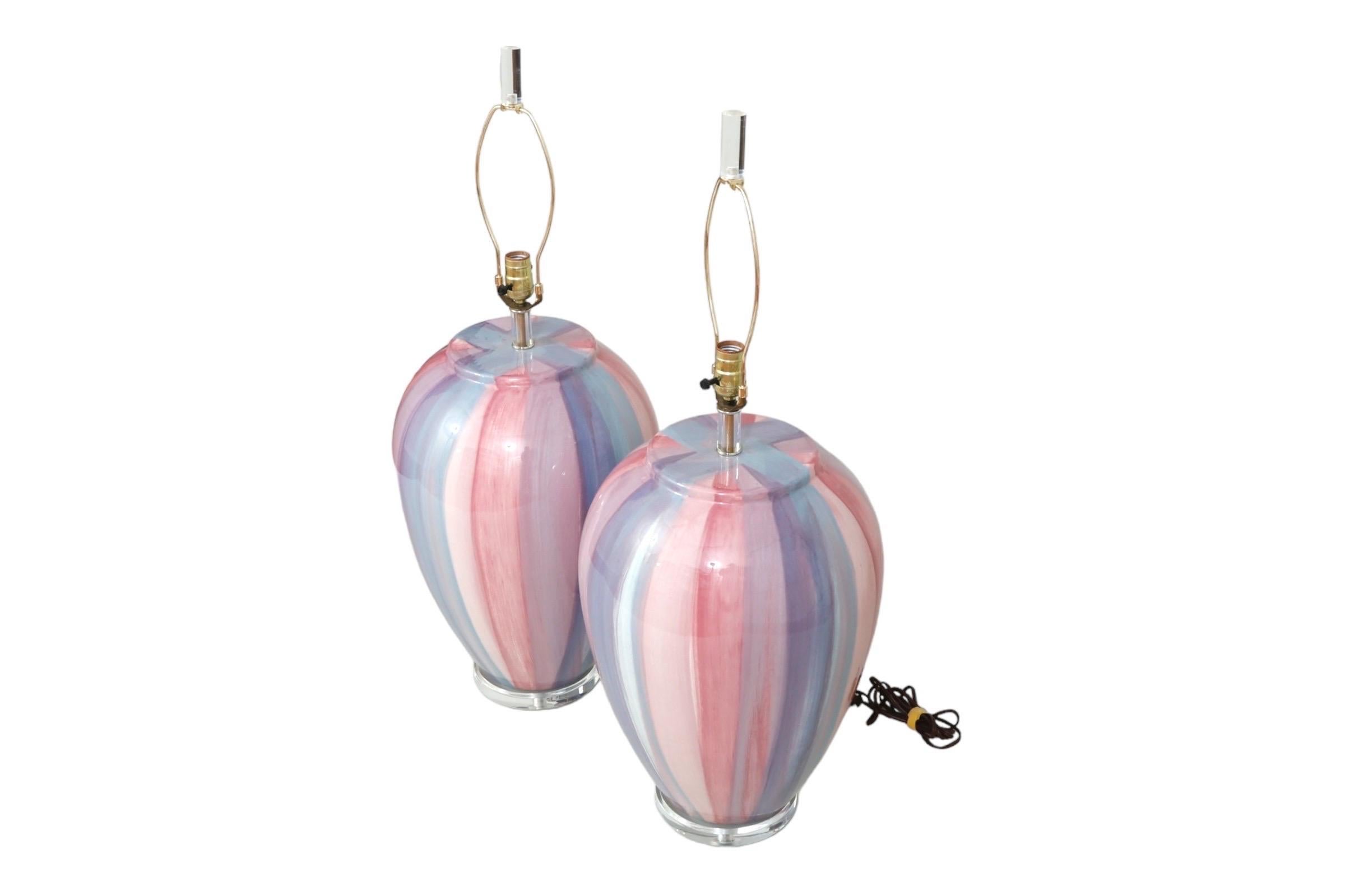 A pair of ceramic and Lucite table lamps by John Richard for Sunset Lamps. Ceramic vases are painted with stripes in candy floss hues of pink, blue, white and purple, above round Lucite bases. Brass sockets on Lucite columns support brass harps