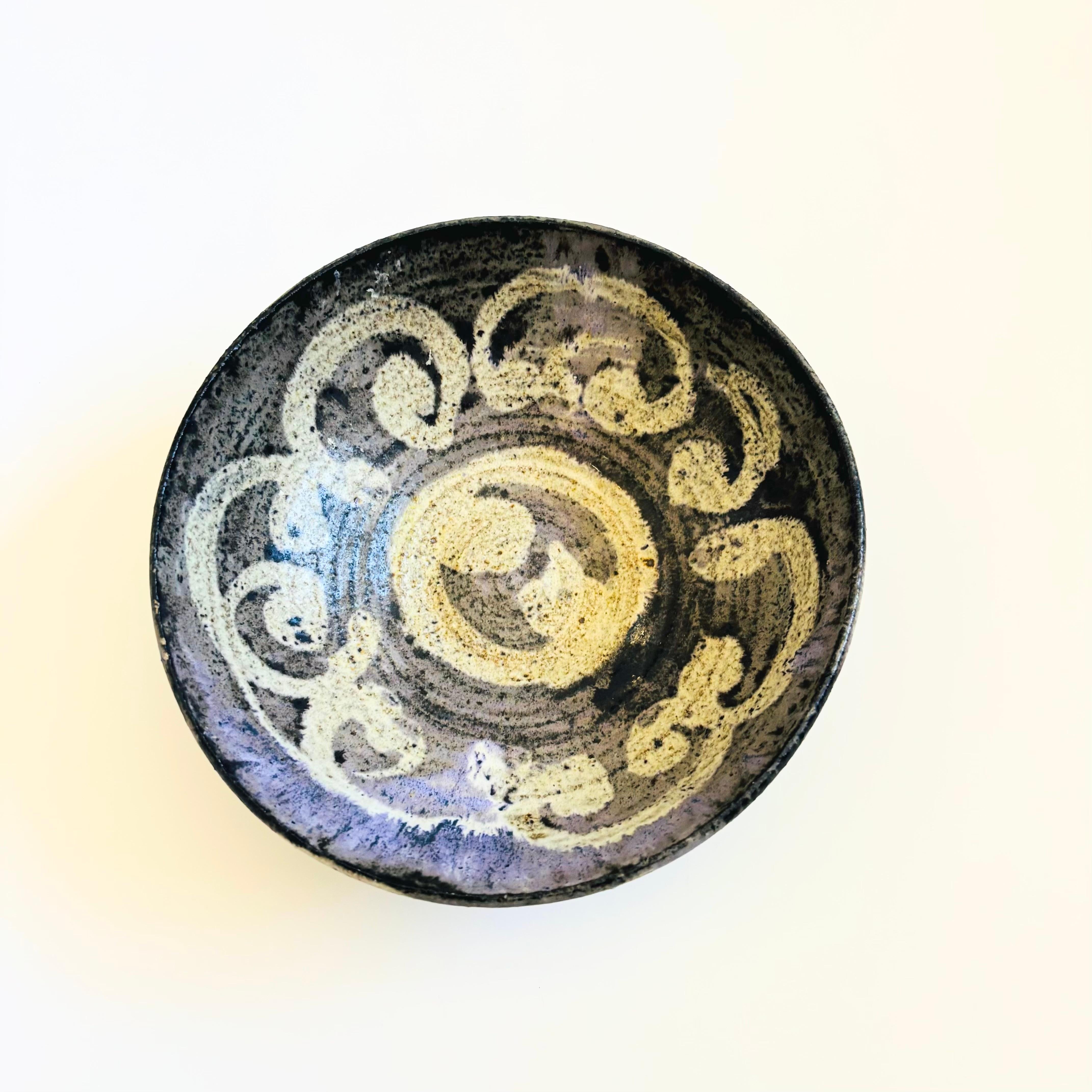 A vintage studio pottery bowl. Speckled gray, dark purple, and black glazes and a hand painted looped design to the inside and outside. Signed on the base 