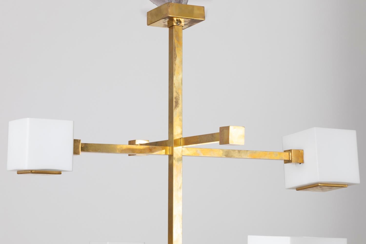 Gilt brass chandelier with eight lights with glass cubes shape. Rectangular central structure around which two brass sticks cross each other, four times: one with two ends formed with little brass cubes, the other one formed ending each side with