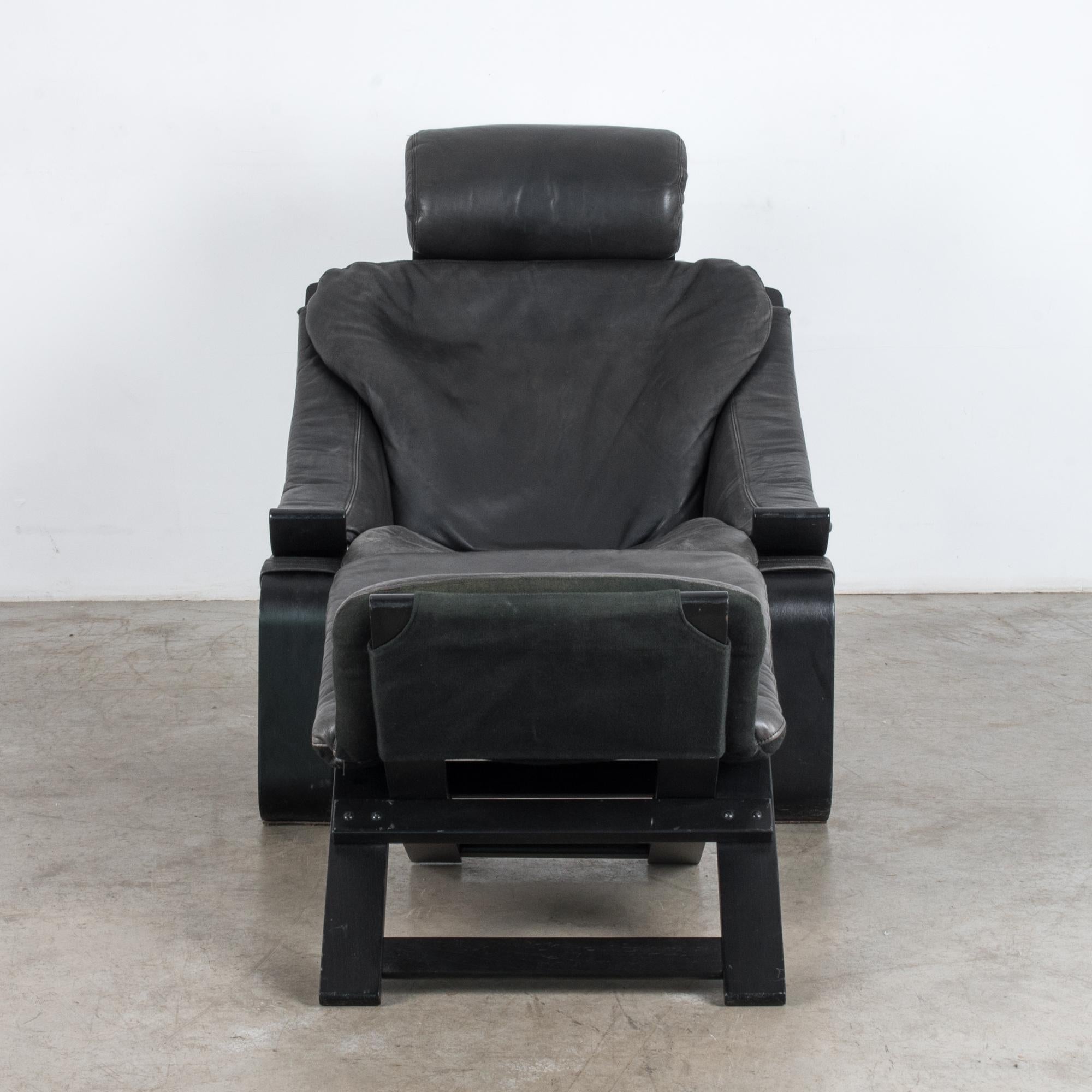 A black leather Kroken armchair from Sweden, circa 1970, with accompanying ottoman. A cantilevered black frame supports a seat of black leather. The deep hollow of the seat, low curves of the armrests and reclined shape conspire to invite a position
