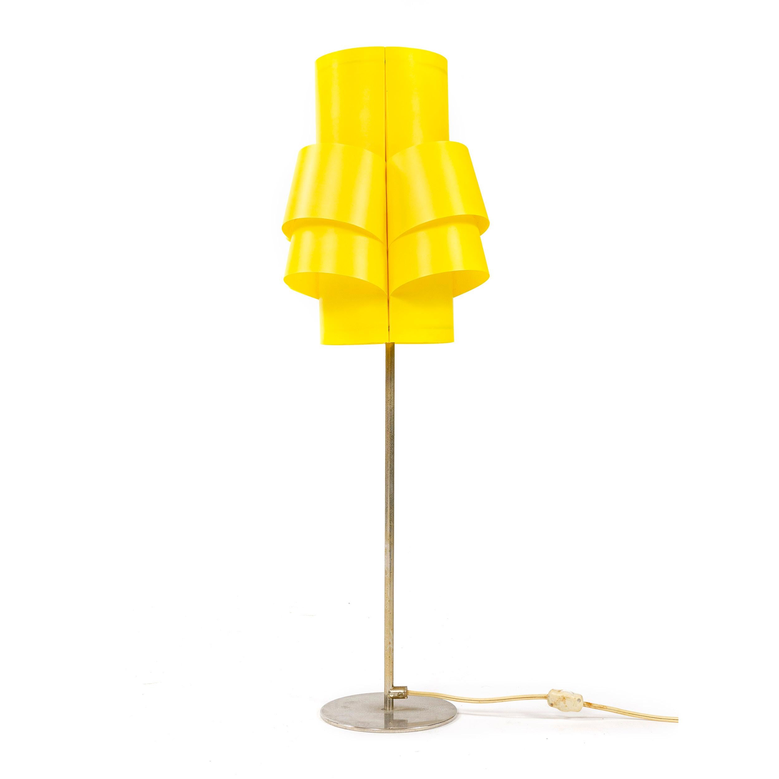 An electric lighting device having a shade of folded and formed yellow plastic attached to an inner wire frame threaded on to its electrical socket. It’s chromed metal base having a slender stem threaded into a circular weighted base with a separate
