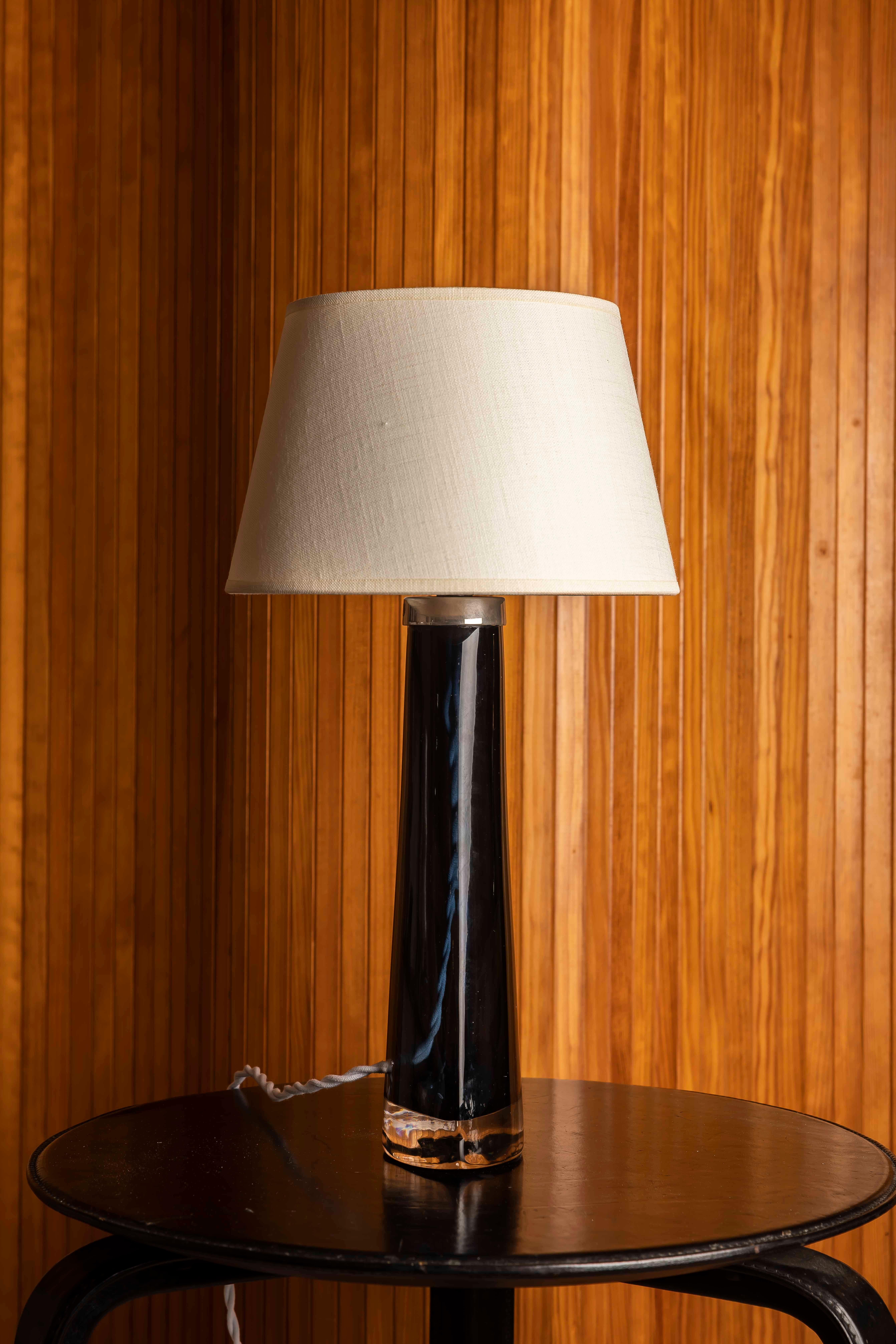 Elegant Swedish table lamp in handblown glass, produced by Orrefors in the 1970s. The piece features a deep cobalt-blue body encased in clear crystal, forming a tapered, faceted silhouette that reflects the precision and restraint of Scandinavian