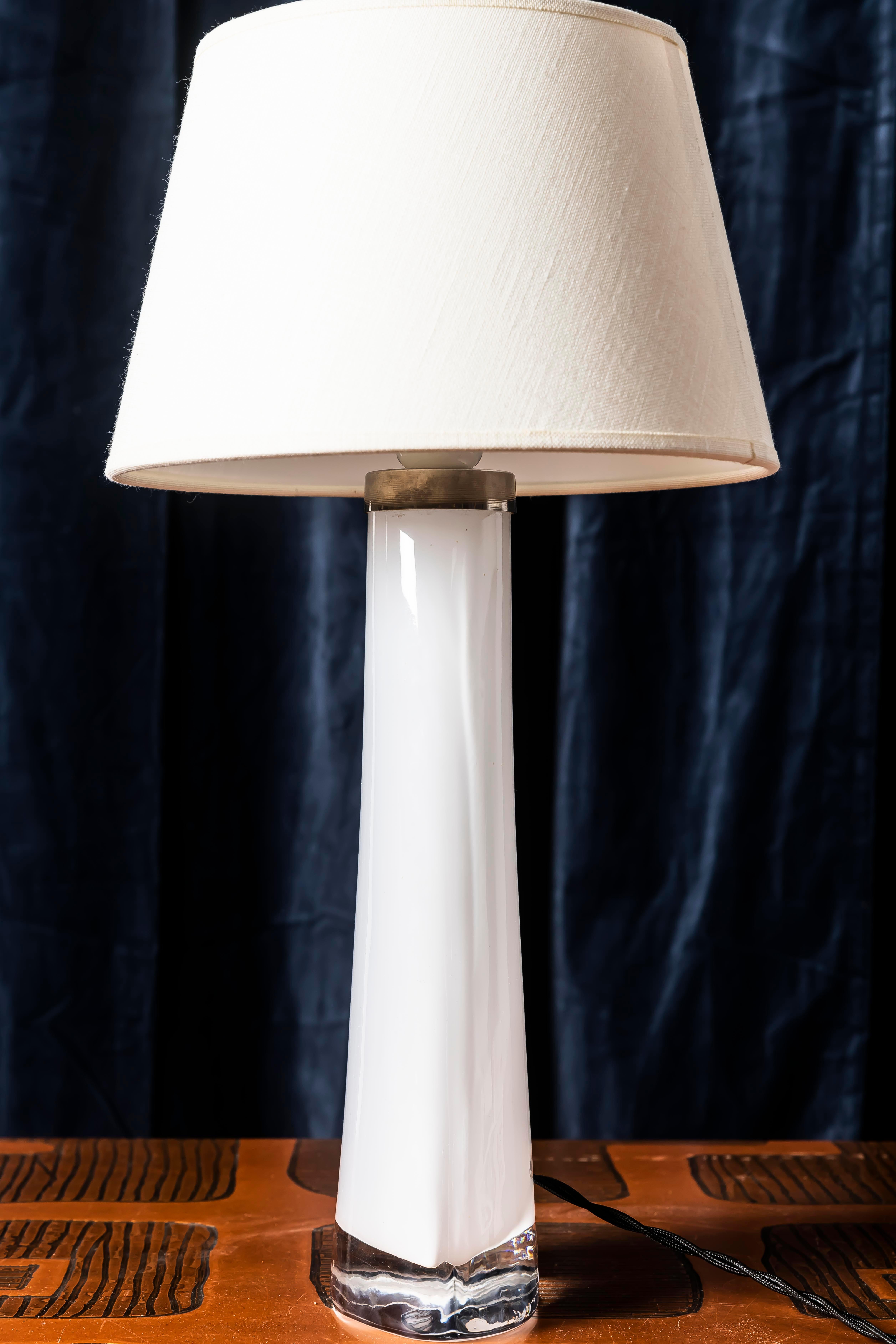 Refined Swedish table lamp in handblown glass, produced by Orrefors during the 1970s. The lamp features a milky white glass core encased in clear crystal, creating an elegant visual balance between opacity and transparency — a hallmark of