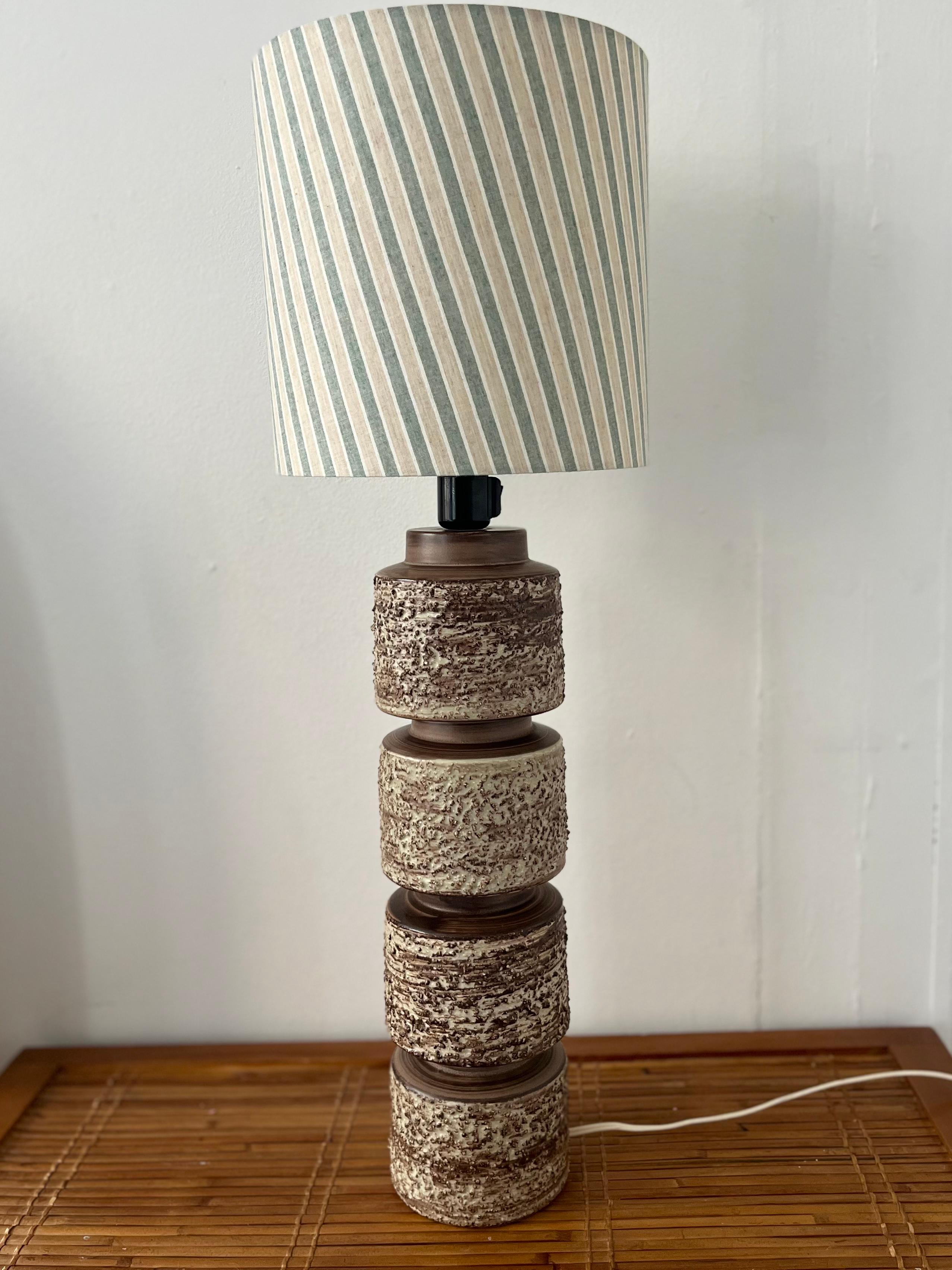 Tall and impressive, this ceramic table lamp was made in Denmark in the 1970s. The look is quite sculptural, making it more than just a lamp. The base is matte ceramics, and the four sections is decorated in a sort of lava glaze. 
It is in perfect