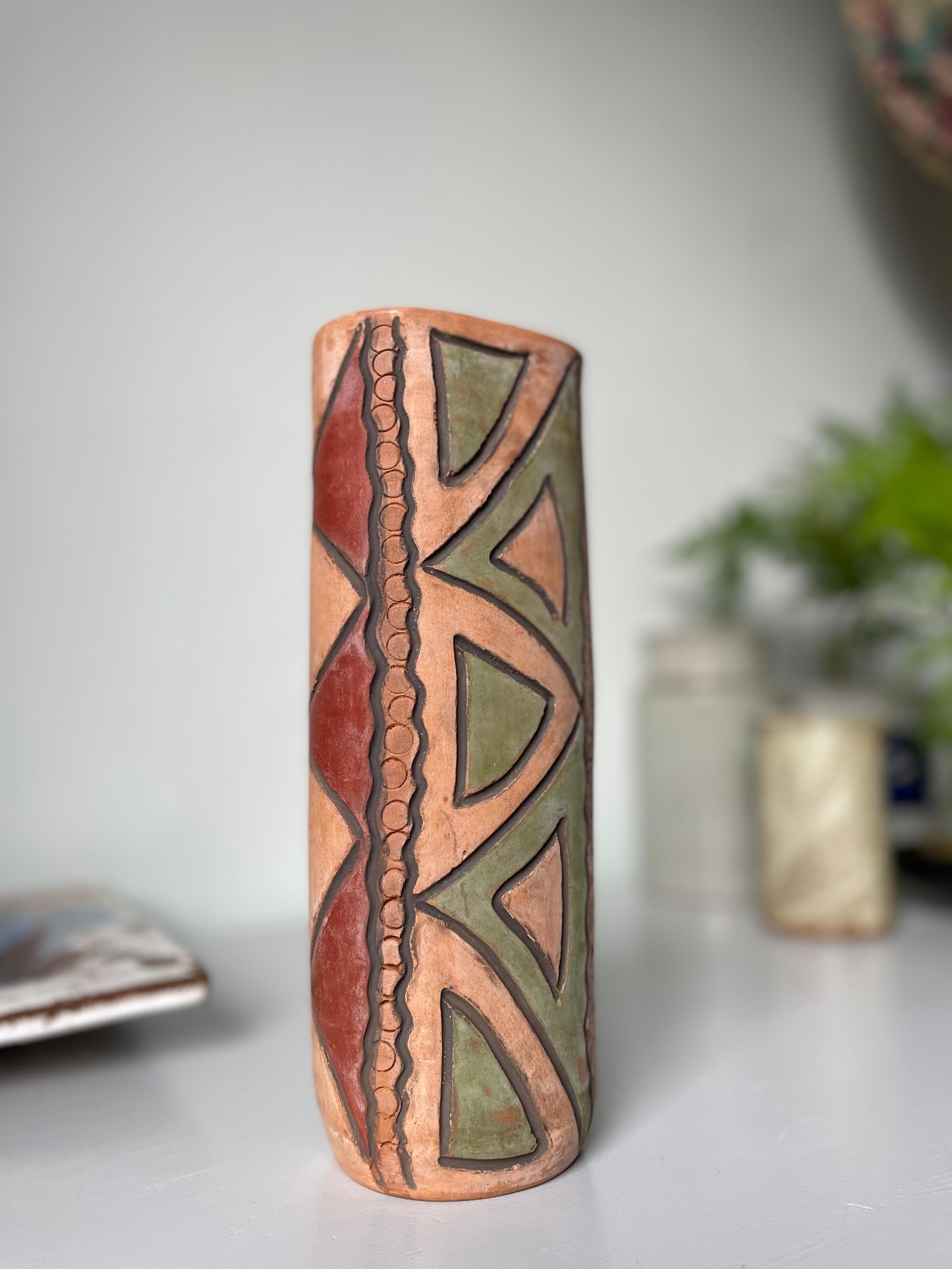 Unusual tall folkloristic ceramic earth toned vase with hand-carved geometric decor. Triangular burgundy and dusty green shapes on earth colored base with circular relief pattern and black wavy lines along the sides. Signed under base. Beautiful