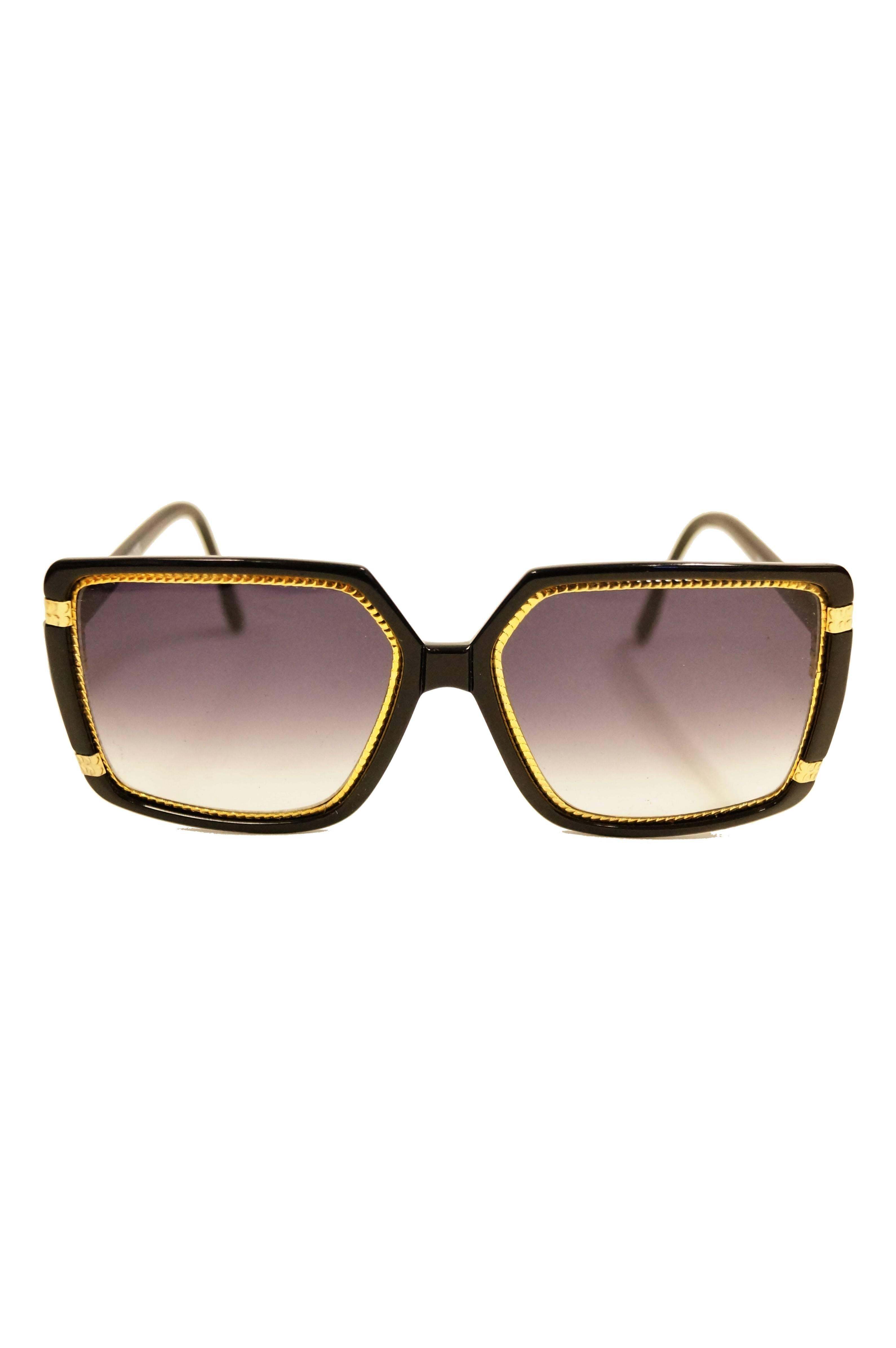 Striking Ted Lapidus black and gold sunglasses. Sunglasses feature a primarily black frame with bold gold braid - like details. Smoky purple to clear gradient on lenses. 

Lens Width- 63.5mm
Bridge Width- 6.35mm
Temple (arm) Length - 127mm

