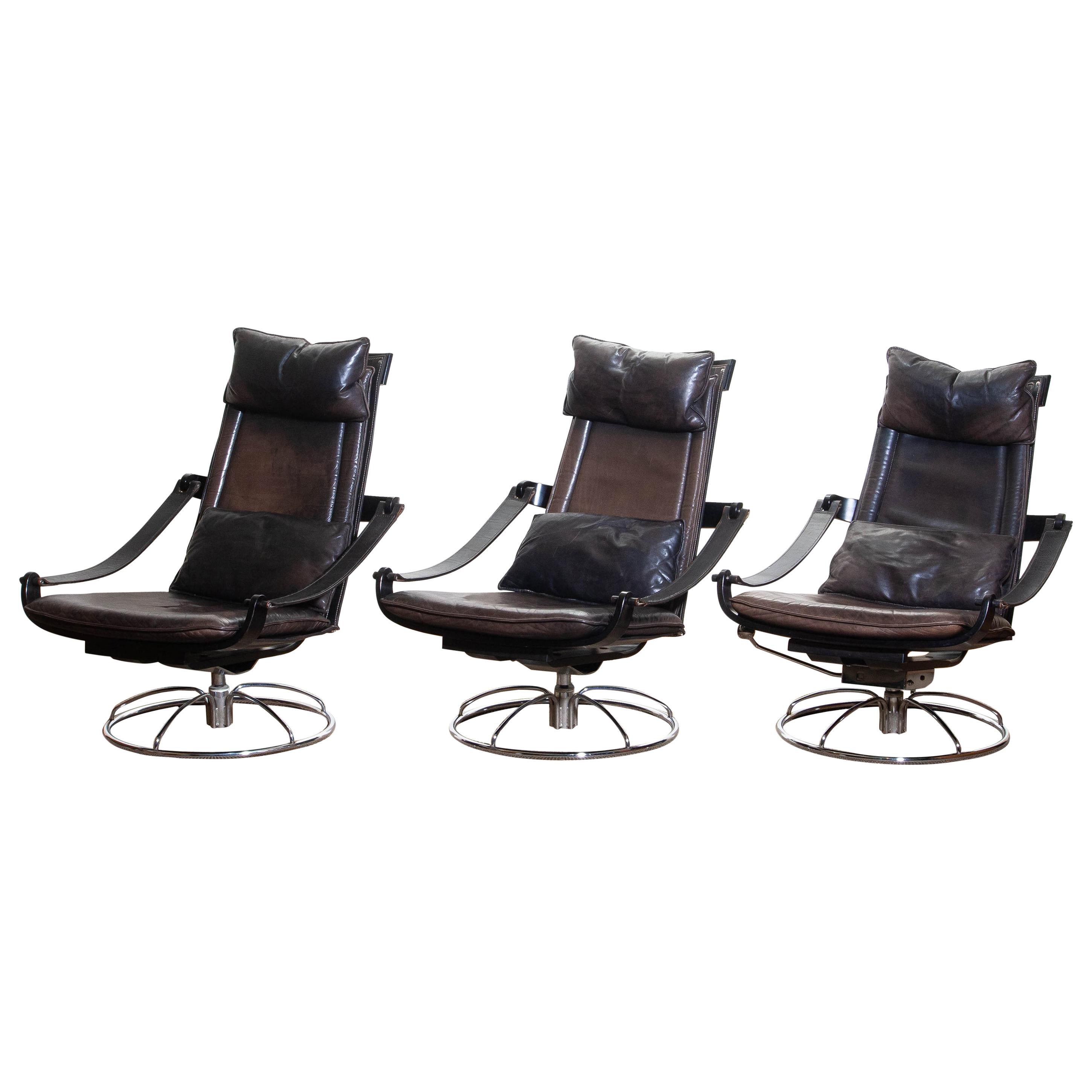 Extremely beautiful and artistic set of three swivel easy / lounge chairs designed by Åke Fribytter for Nelo, Sweden.
These high quality chairs features a plywood frame and brown leather cushions and a chromed metal base.
One chair has got an