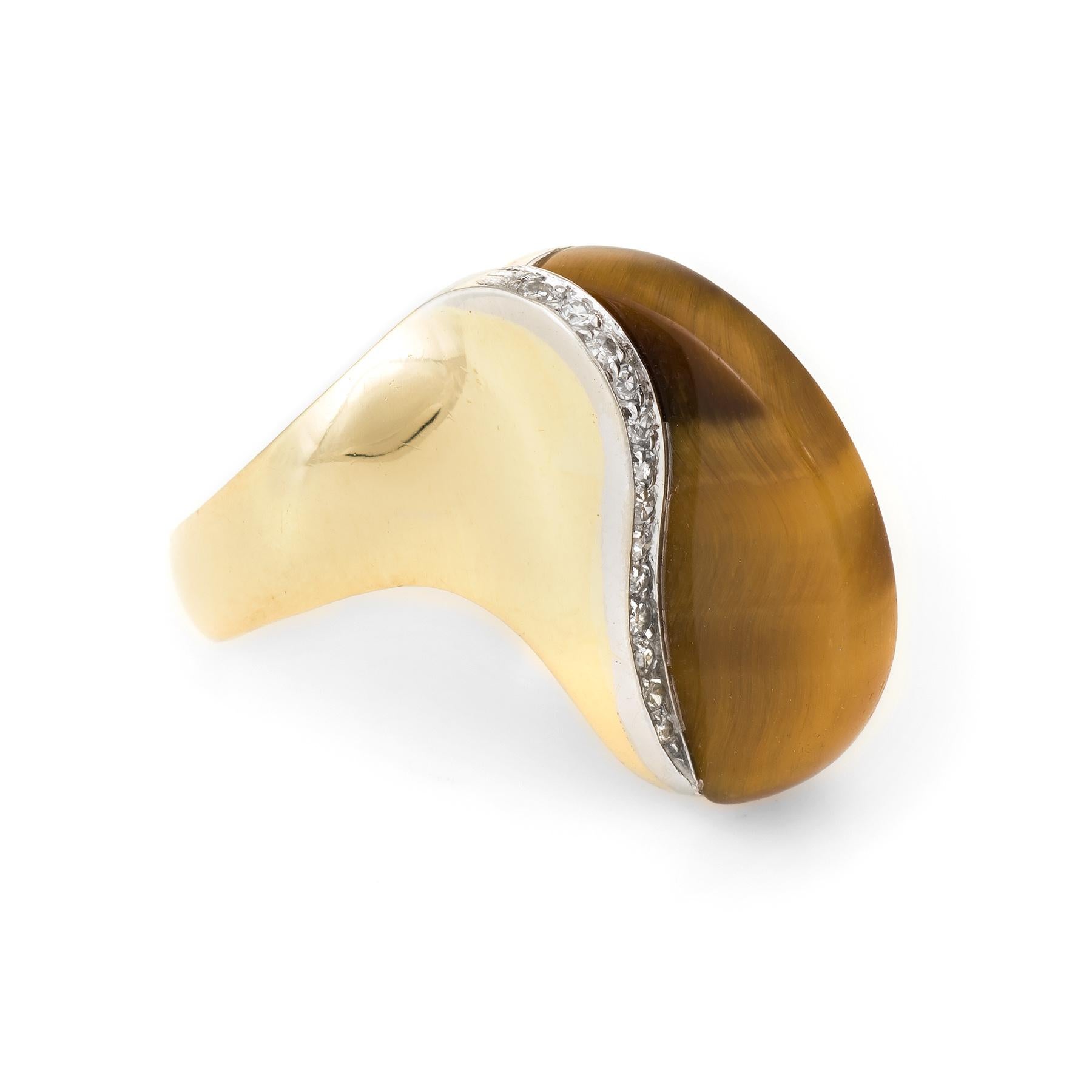Distinct vintage cocktail ring (circa 1970s), crafted in 18 karat yellow gold. 

Centrally mounted high dome tigers eye measures 21mm x 3mm, accented with an estimated 0.26 carats of diamonds (estimated at G-H color and VS2 clarity). The tigers eye