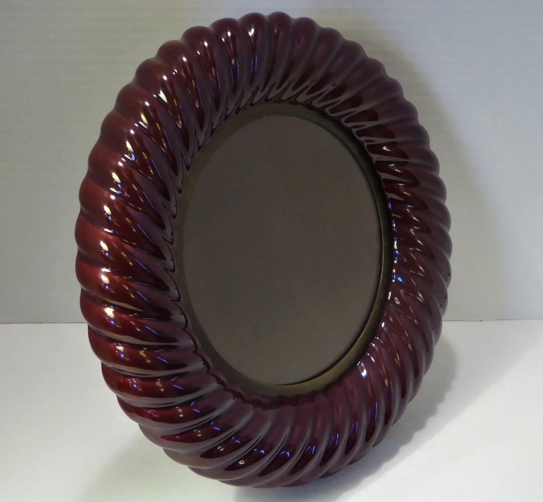 This Italian 1970 Tommaso Barbi picture frame has a wonderful plum color. With his famed ceramic rope form, it is circular with an inset brass and glass. Signed in the brass on the back, it has a supporting leg for display.
Brass with age patina,