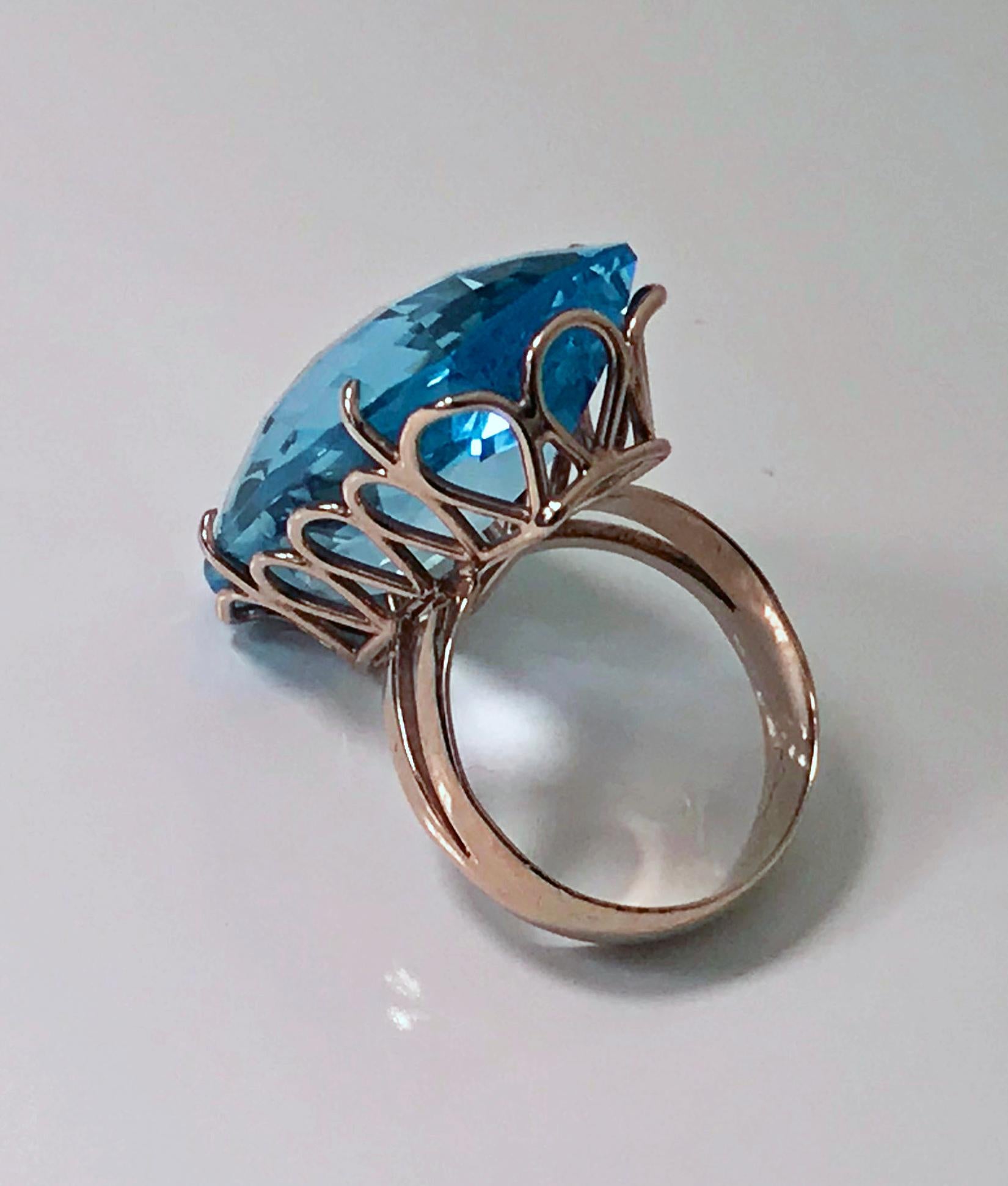 Topaz and Gold custom Ring C.1970. The 14K rose gold ring set with a large cushion oval shape medium dark, strong intensity blue topaz, gauging 35.00 x 14.80 x 10.00 mm, approximately 53.57 cts, VVS clarity, good cut. The mount of a custom tear drop
