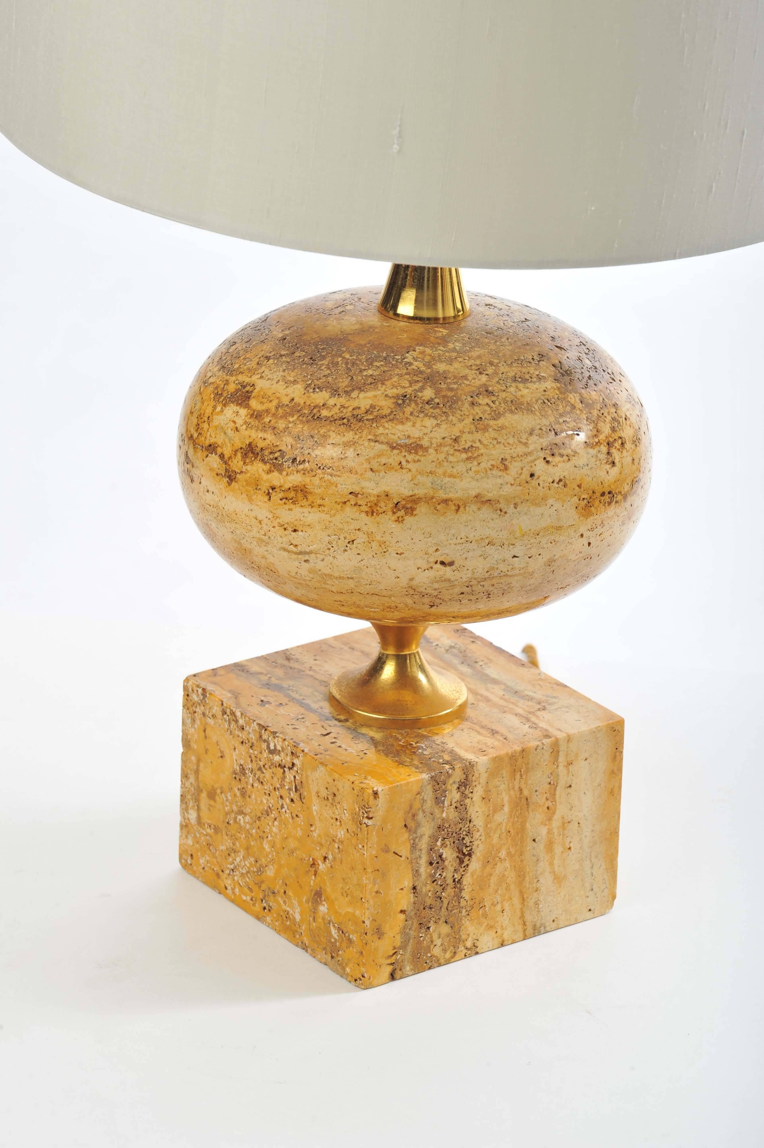 Curvaceous lamp in polished travertine stone, build up in layers of cream, orange, rusty brown tones, created from the geothermal springs. The travertine contrasts well with the brass supports and the cream silk lamp shade.
The width of the solid