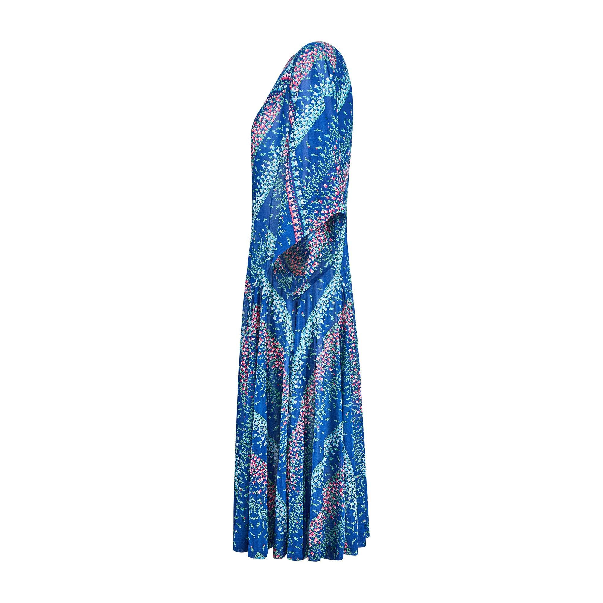 Robe d'été des années 1970 fabriquée en Italie par Travona. Le tissu est un jersey léger de crêpe bleu royal à motifs de feuillage vert, de bourgeons rose pâle et fuchsia et de fleurs bleu layette. Il présente une silhouette fluide typique de