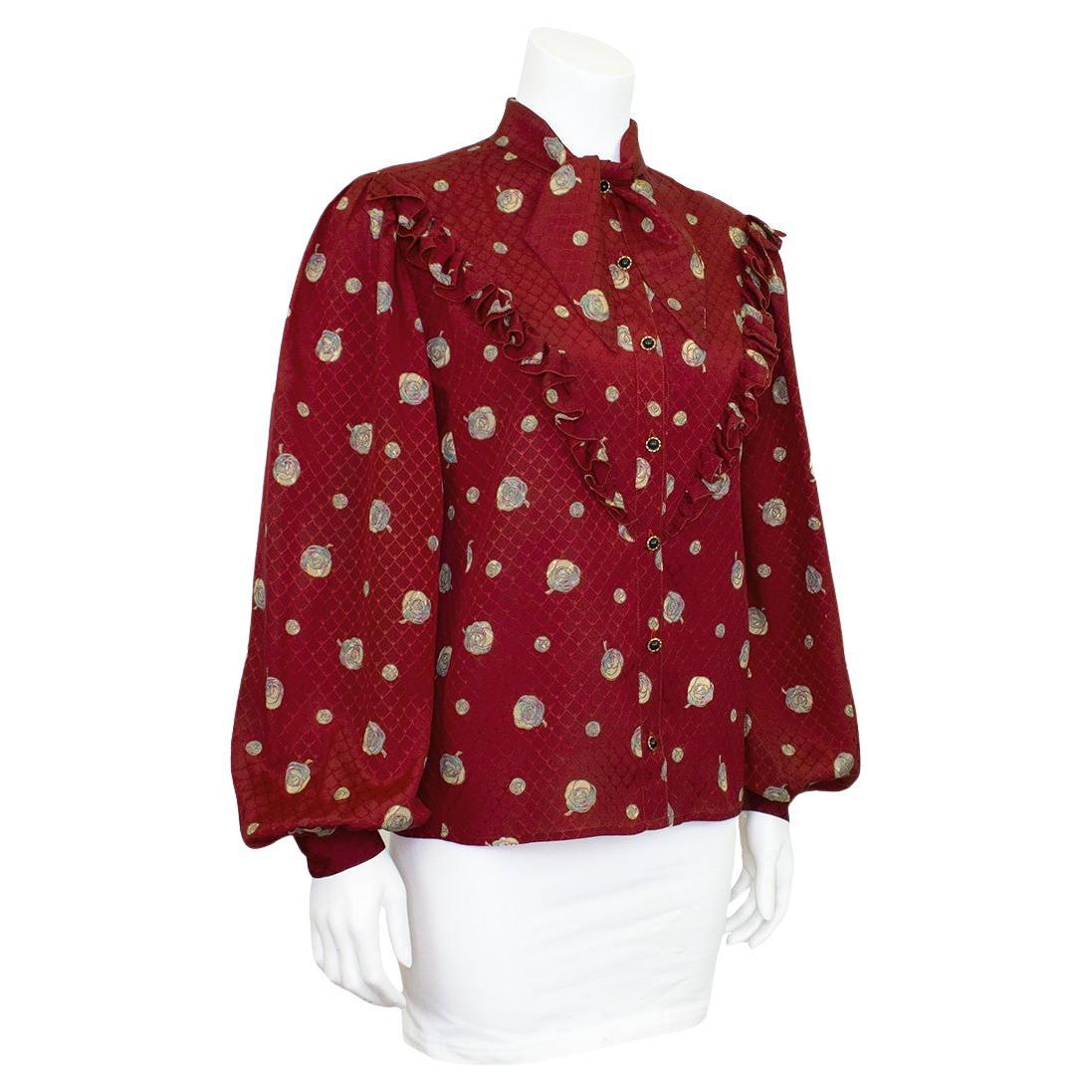 Klassische Seidenjacquard-Bluse in Bordeau mit Rüschenpasse in V-Form und Selbstbinder im Nacken. Knopfleiste und geraffte Ärmel mit Knopfmanschette. Cremefarben mit einem Hauch von mintfarbenem Gardenien-Print auf dem gesamten Stoff, mit schwarzen