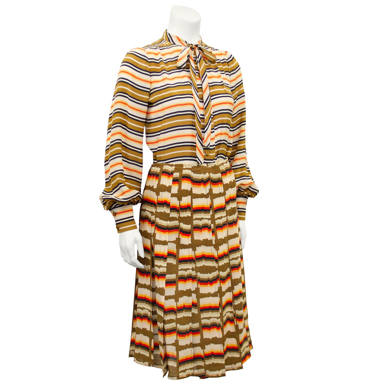 1970s Emanuel Ungaro blouse and skirt ensemble. Blouse features horizontal stripes in beige, brown, black and orange, bishop sleeves and a thin pussy bow tie . The skirt features the same colour story with a distorted horizontal stripe. Skirt is