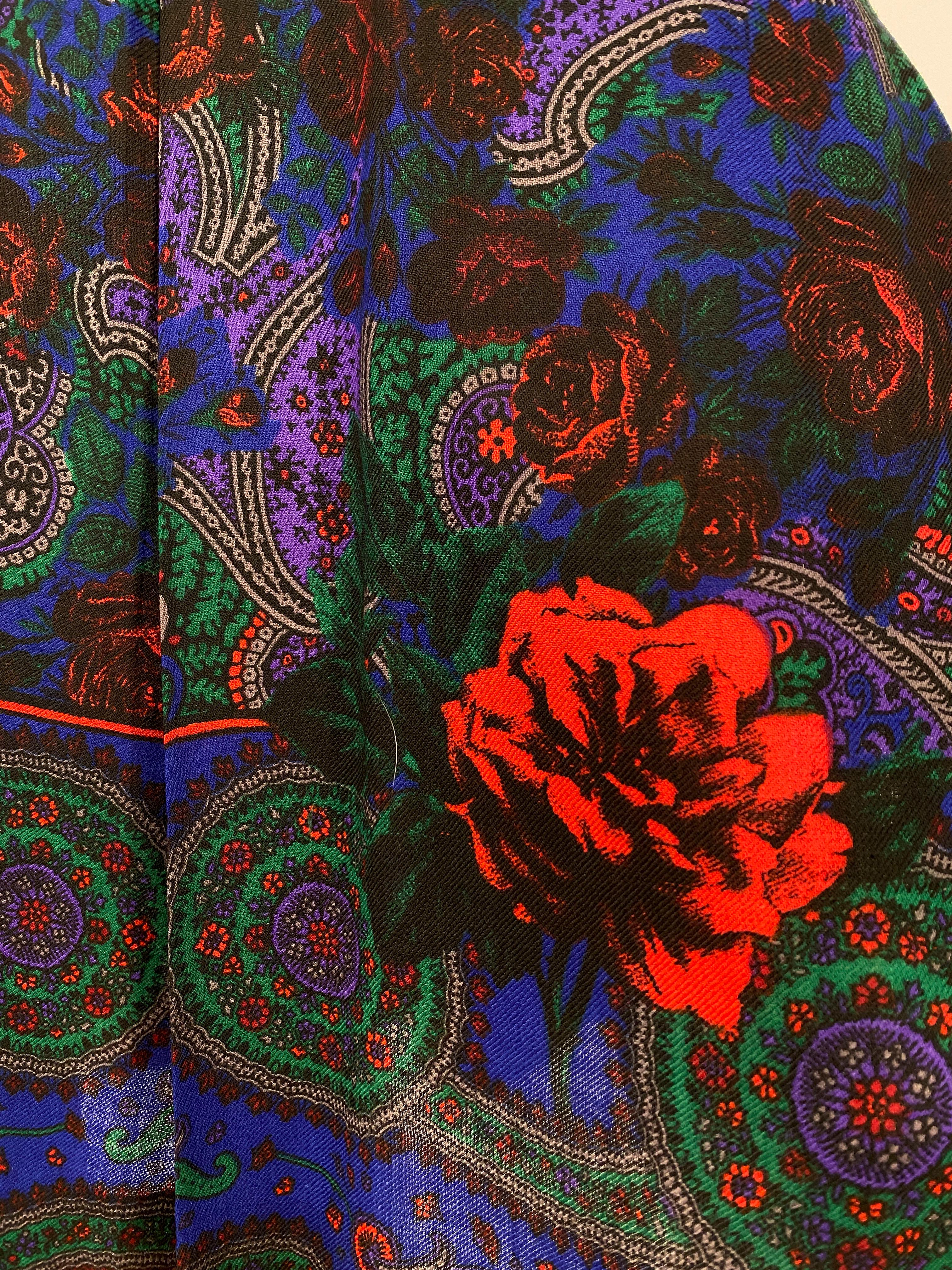 rock aus feiner Wolle aus den 1970er Jahren mit einem farbenfrohen Rosendruck auf tief königsblauem Hintergrund. An den Seiten befinden sich 4 tiefe Falten, die an der Hüfte beginnen. Der seitliche Reißverschluss ist beim Tragen unsichtbar.