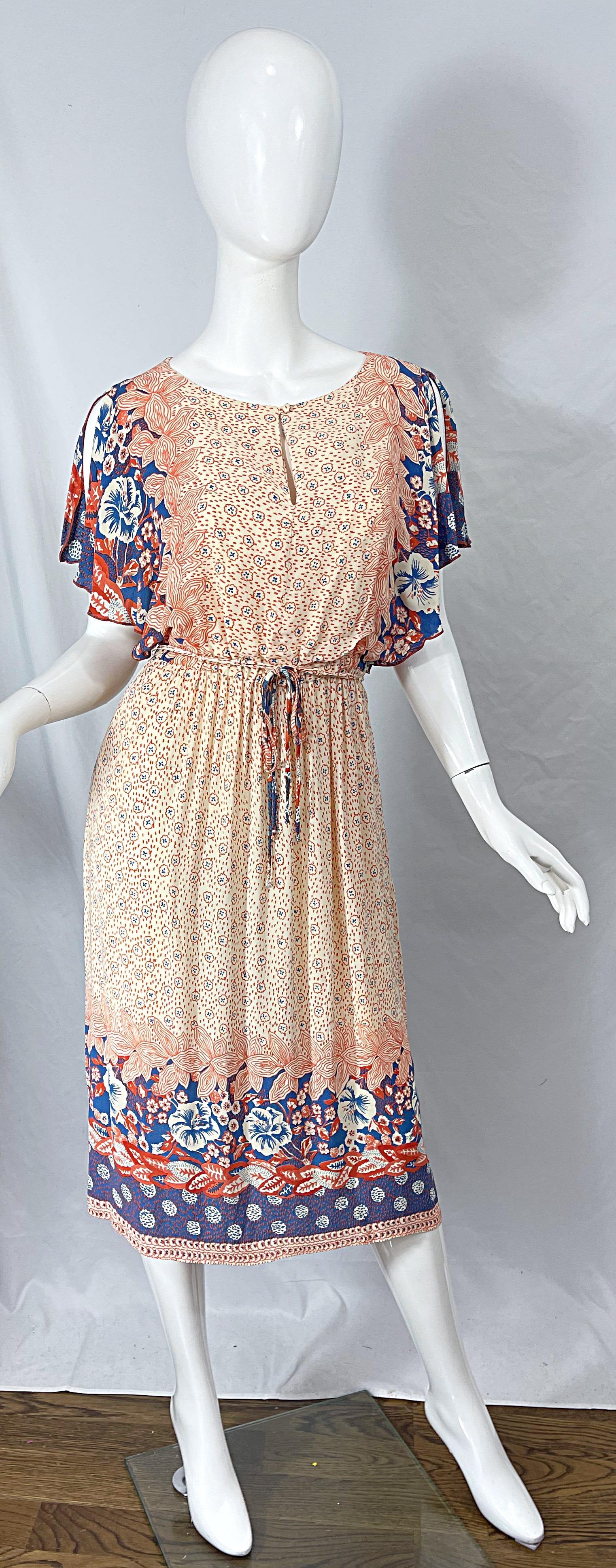 Chic 1970s VICTOR COSTA flower printed cold shoulder boho rayon dress ! Features an ivory backdrop with burnt orange and blue flowers printed throughout. Matching detachable belt can be tied into a bow or left hanging. Elastic waistband makes this
